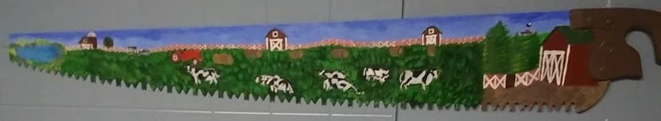 A wooden border with painted farm scene including cows, barns, and greenery.