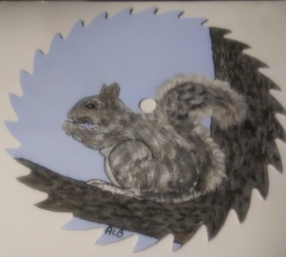 A circular saw blade with a detailed drawing of a squirrel on it, perched on a branch with a blue sky background.