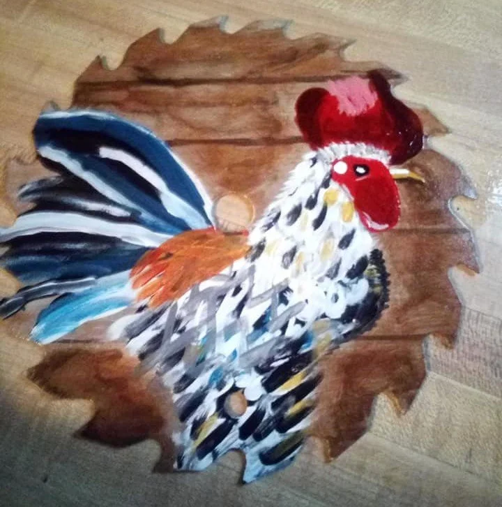 Painted wooden wall decoration depicting a colorful rooster with a red comb and wattle, set against a leaf-shaped brown background.