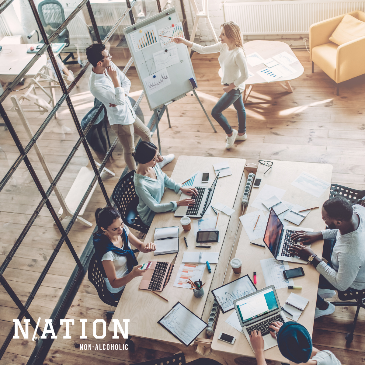 Workers sitting in an office on laptops or standing.
