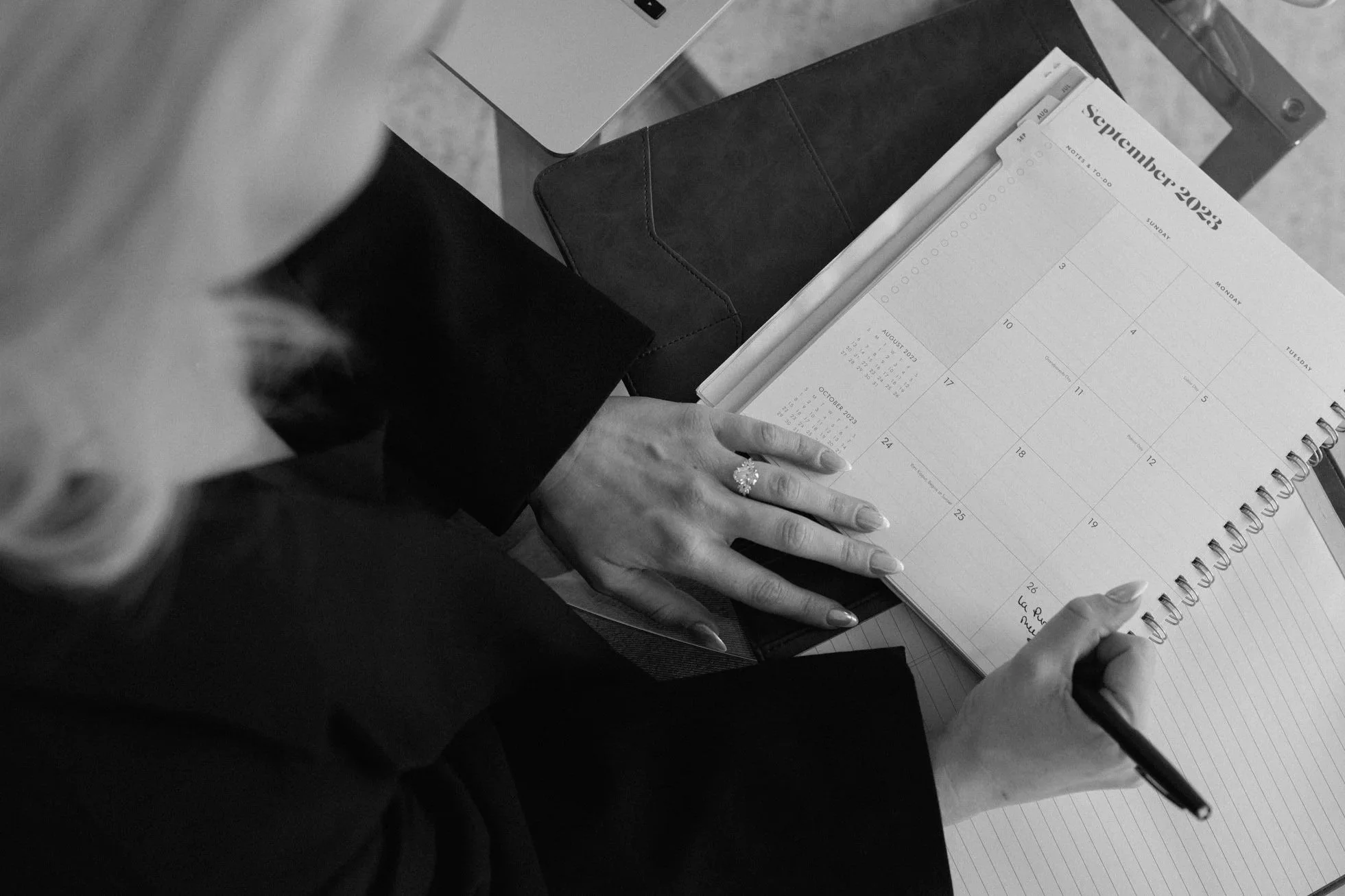 A woman writes in a planner on a desk with a laptop, notebooks, and a cup. The planner is open to September 2022.