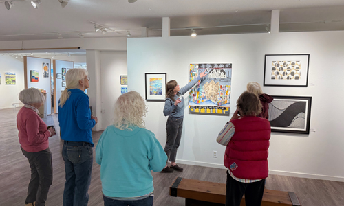 Group of people standing in an art gallery while one points at a painting