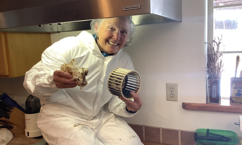A smiling person cleaning grease from a kitchen vent hood filter