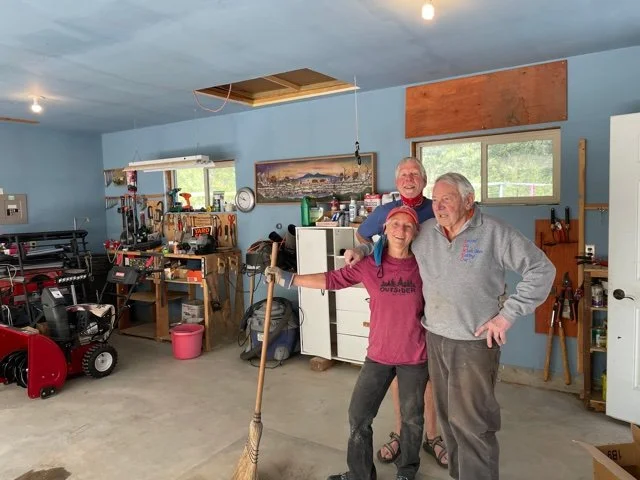 3 people in a garage, one person holding a broom