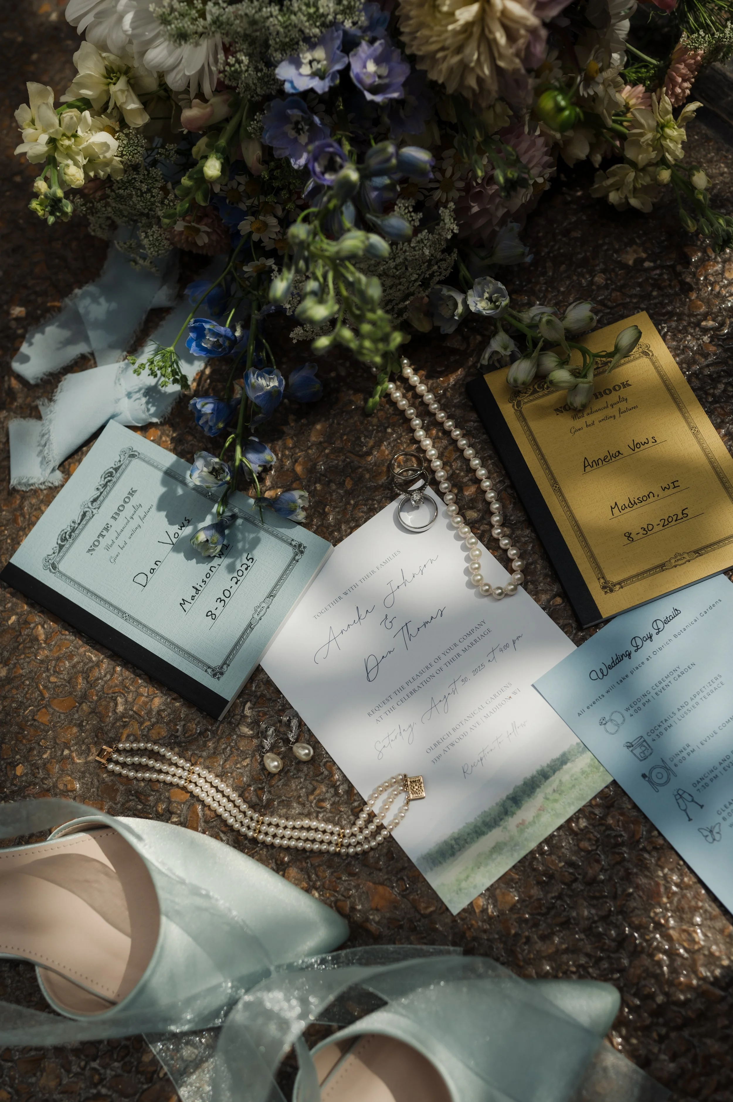 Wedding invitation and program for Amy Johnson and Dan Thomas, wedding details, pearl necklaces, wedding rings, blue shoes, and a bouquet of flowers with white, purple, and green blooms.
