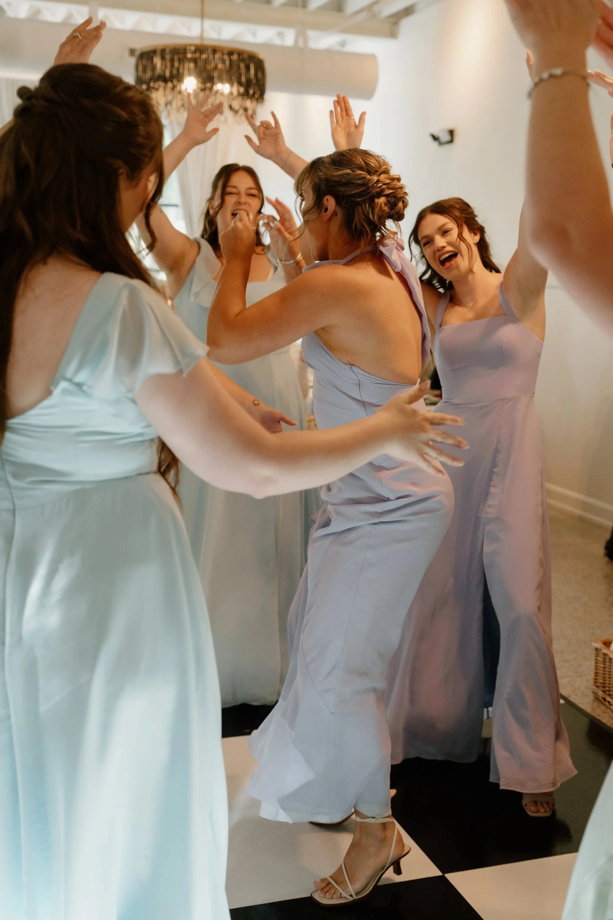 A group of women celebrating at a wedding reception, dancing and smiling in a decorated indoor venue.