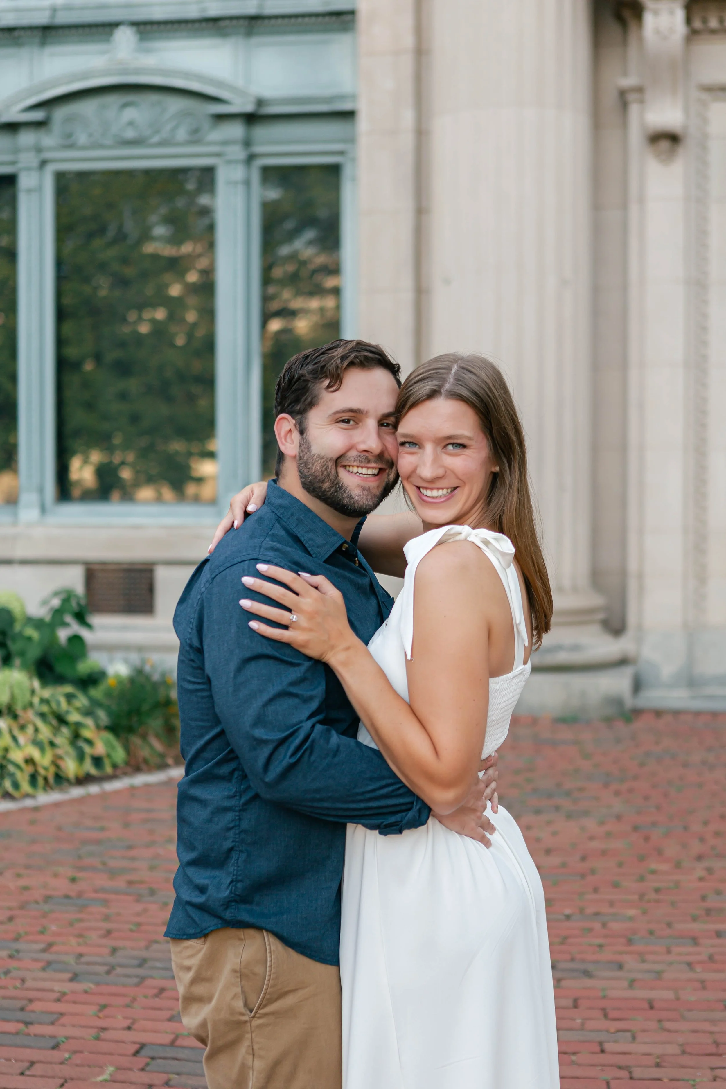 A happy couple embracing outdoors in front of a historic building, smiling at the camera