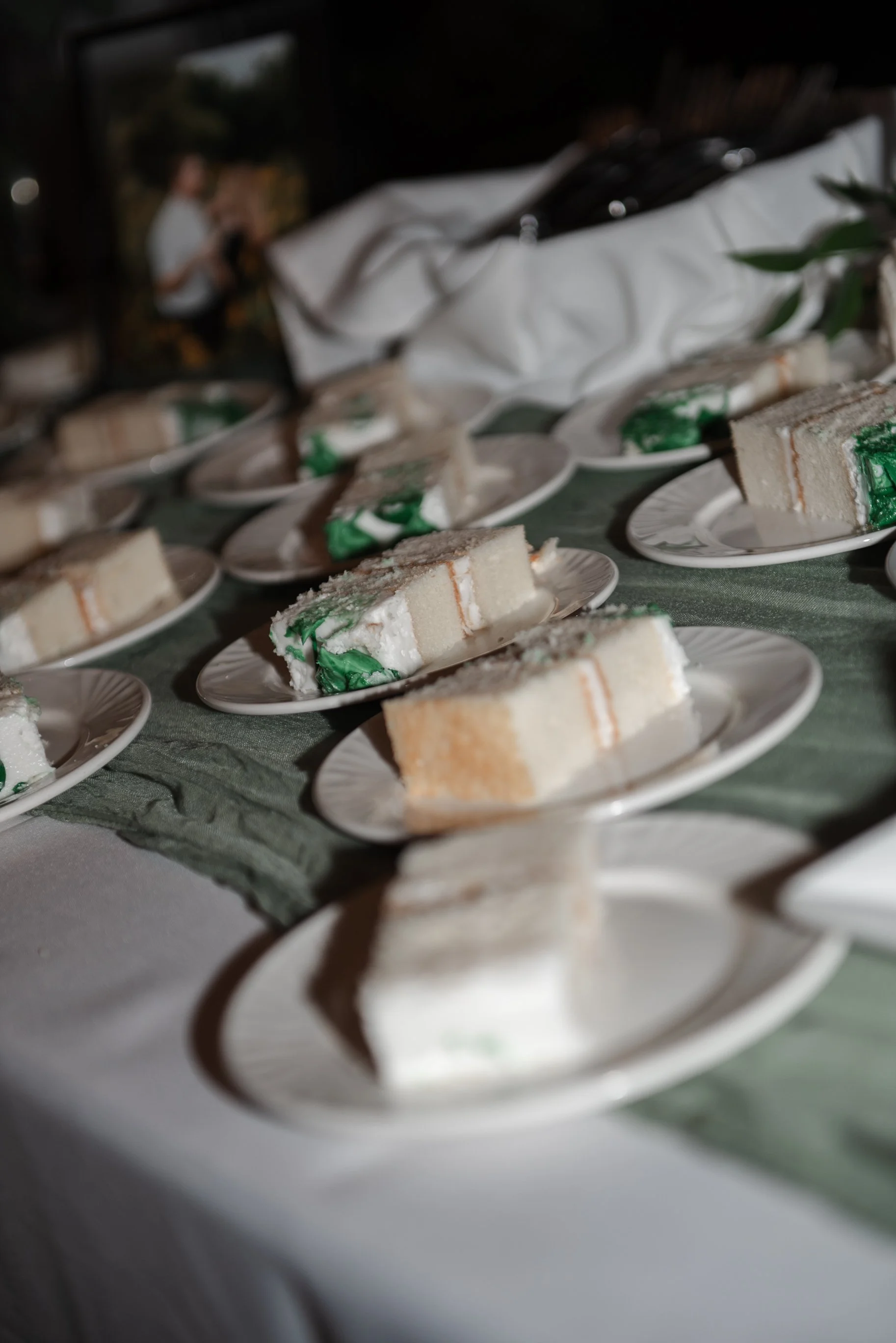 Several slices of cake on white plates arranged on a table with a green tablecloth.