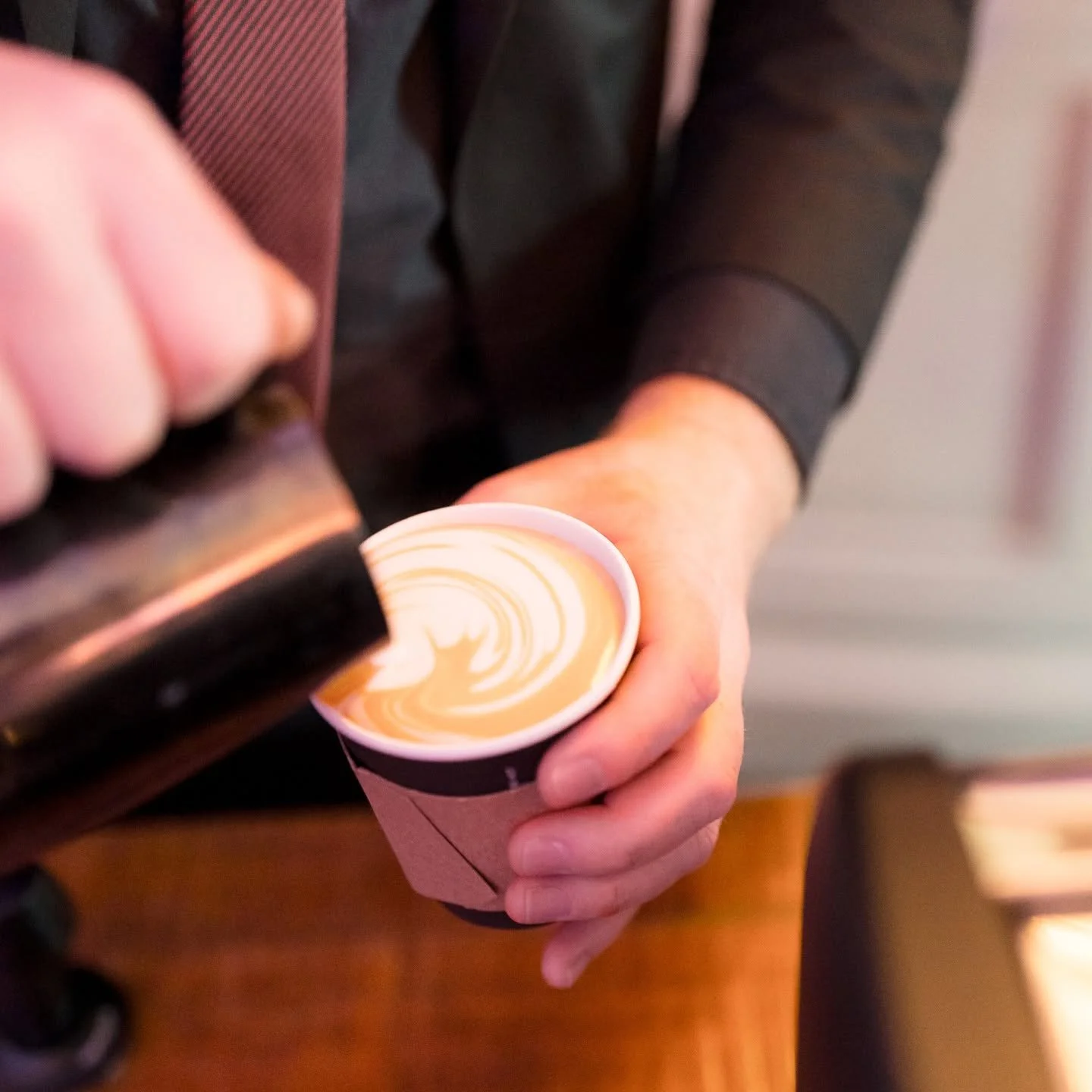 A person pouring caramel syrup into a cup of coffee with latte art, held with one hand.