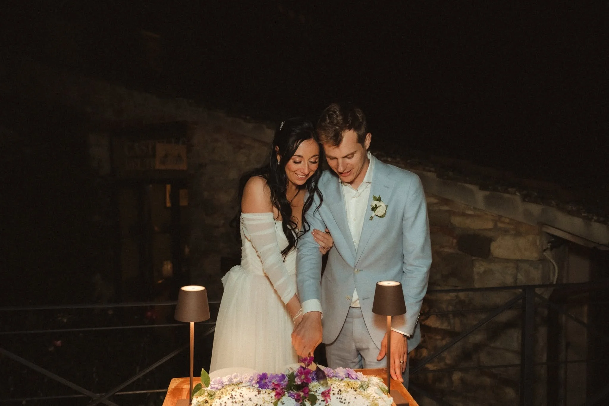 A bride and groom cutting a wedding cake together during their ceremony in a rustic indoor setting.