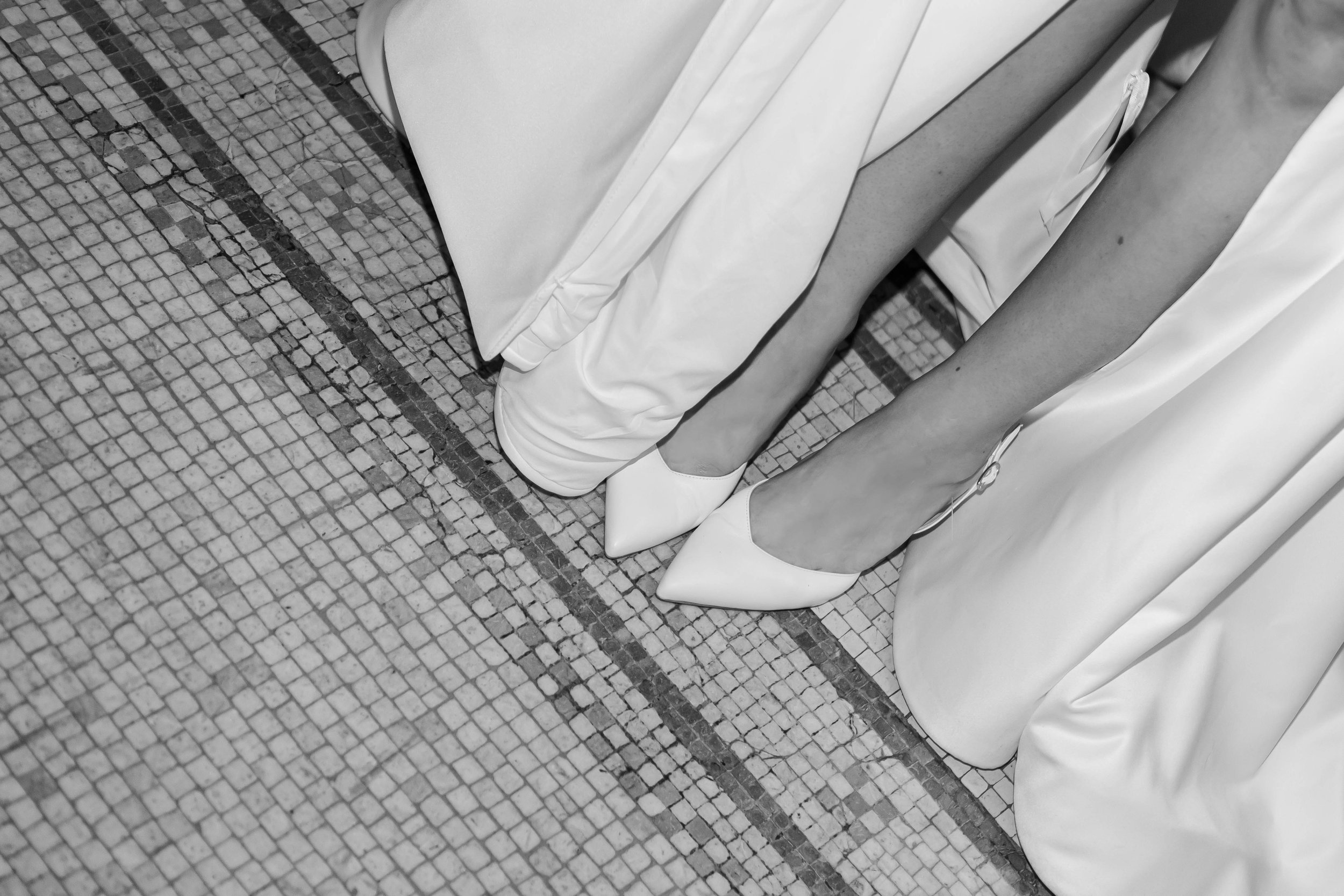 Close-up of a woman in high heels and a long dress, with a man in a suit, standing on a tiled floor.