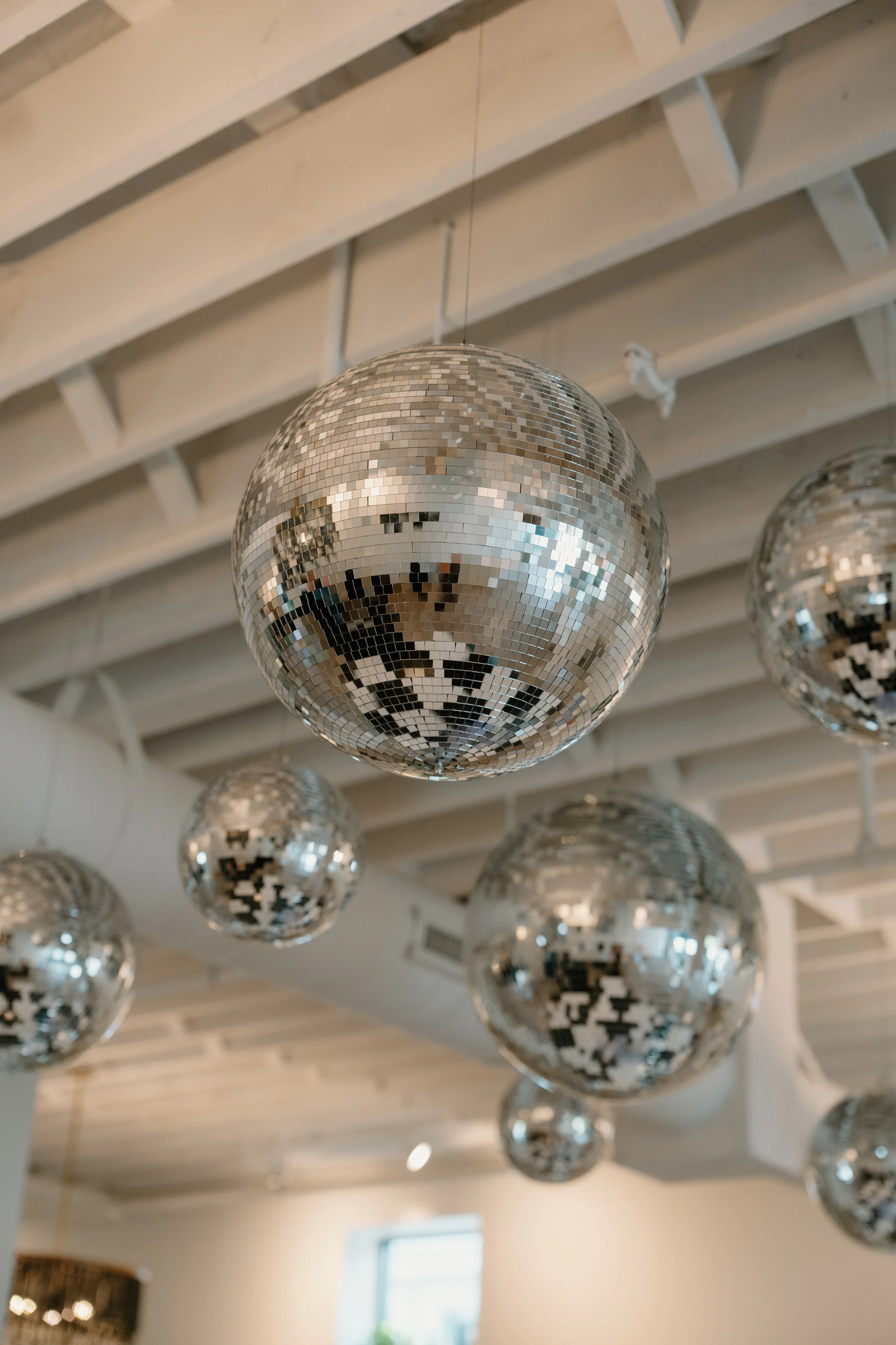 Multiple disco balls hanging from a ceiling with wooden beams in a modern indoor space.