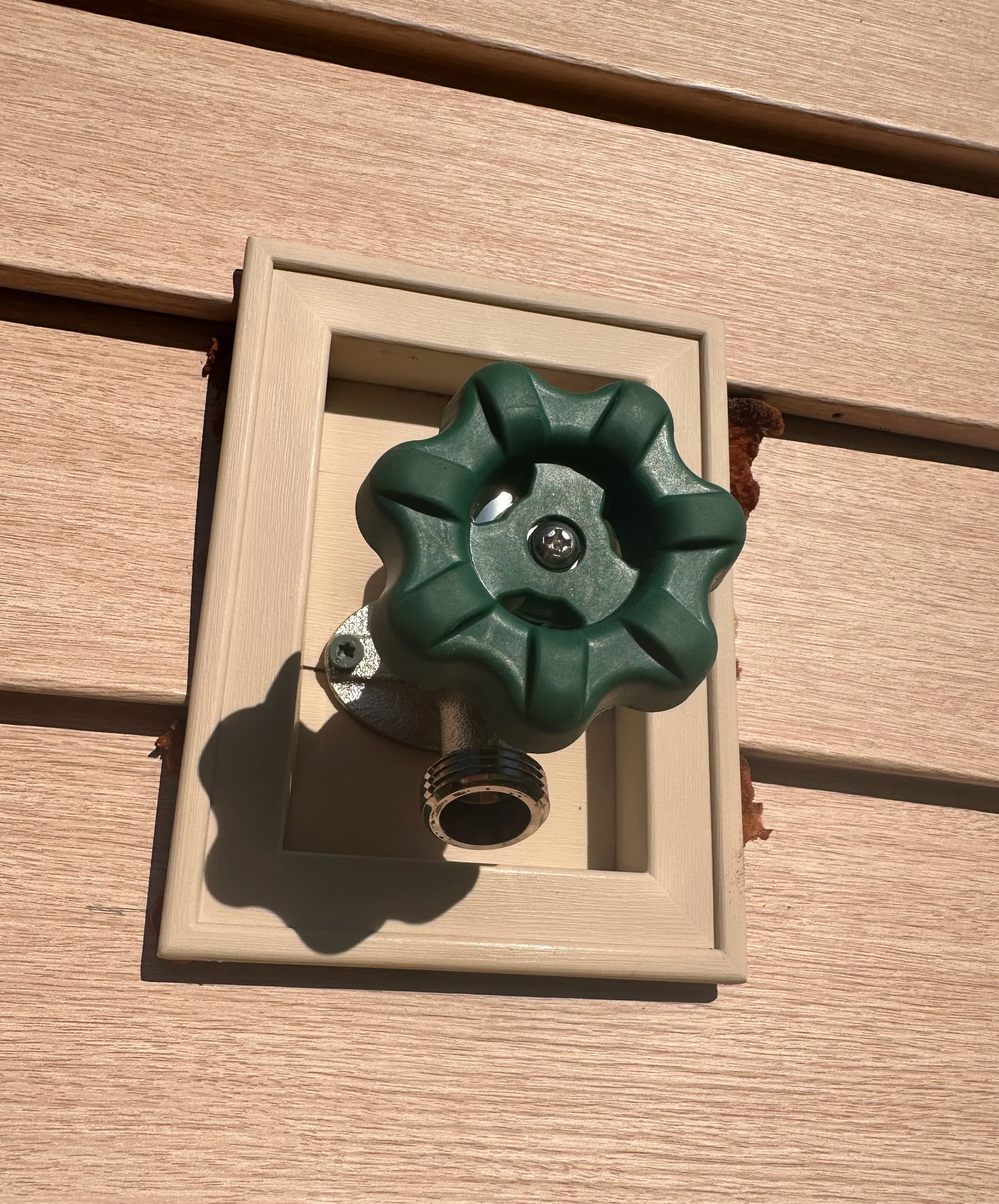 Outdoor view of a green water valve attached to a beige electrical box on a wooden wall.