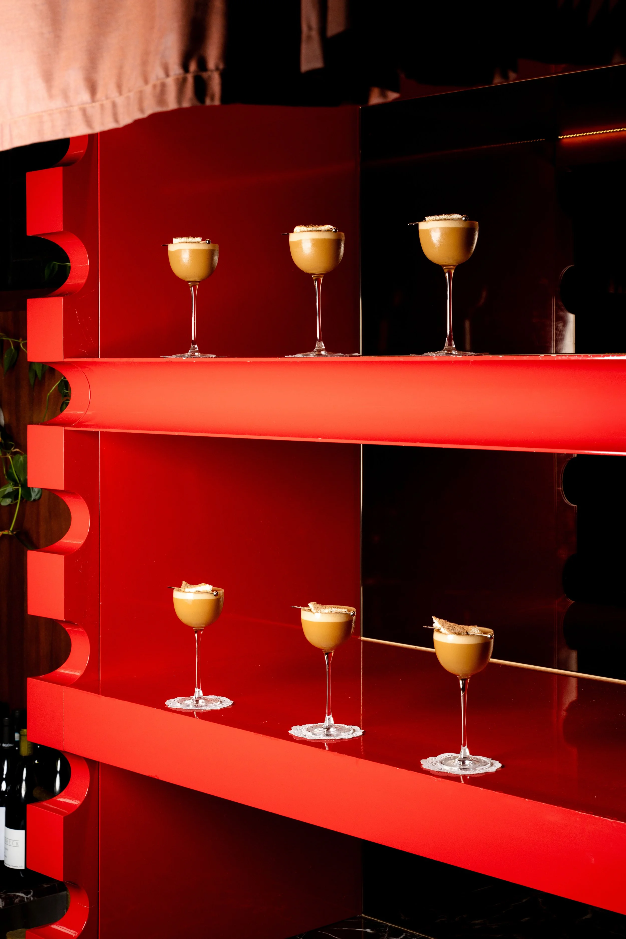 Multiple cocktail glasses with creamy drinks topped with garnishes, arranged on a red and black shelving unit.