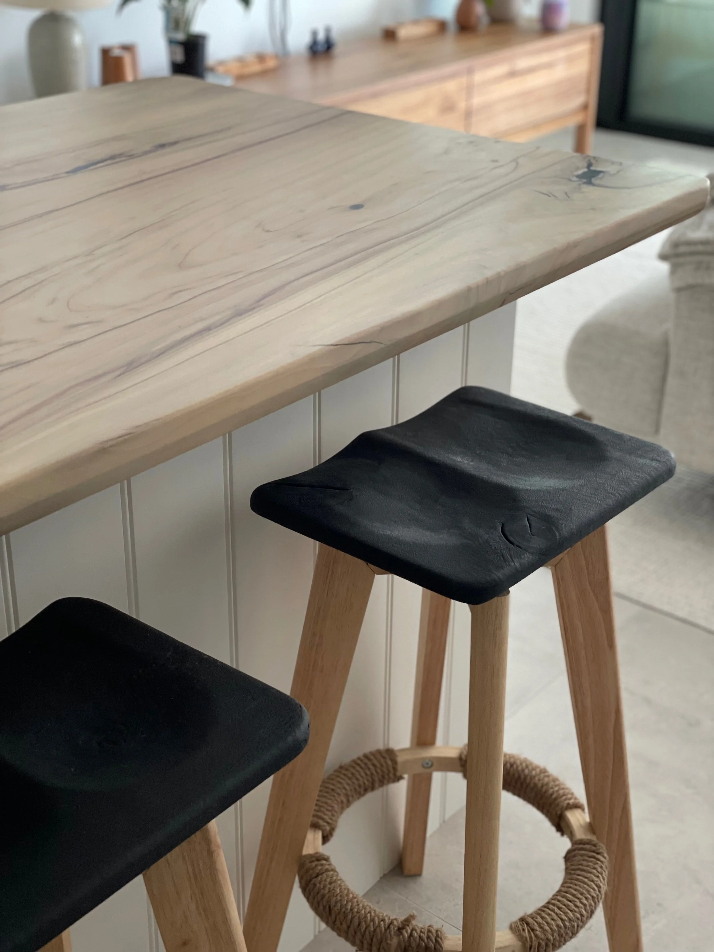 Close-up of three wooden barstools with black seats lined up at a wooden kitchen counter in a modern, neutral-toned kitchen.
