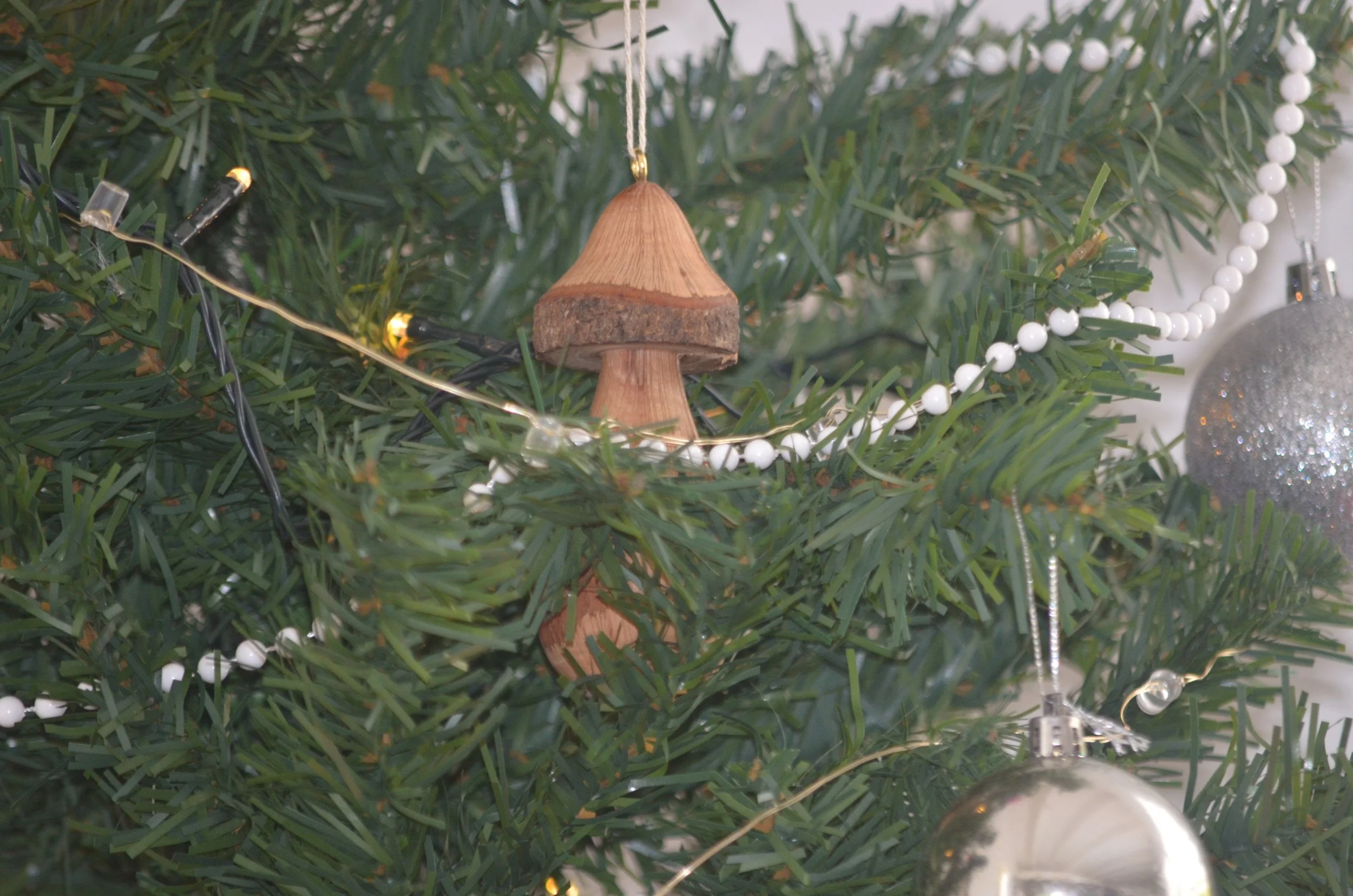 Close-up of Christmas tree ornament in the shape of a mushroom, hanging on a decorated Christmas tree with lights and other ornaments.