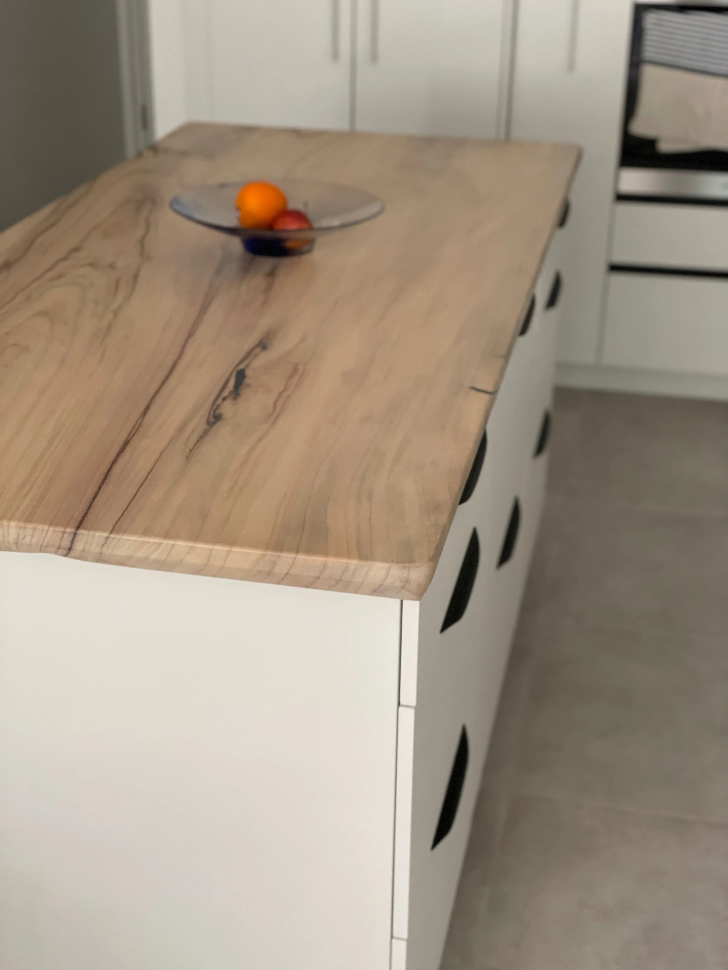 A kitchen with a wooden countertop and white cabinets, a glass bowl with oranges and apples on the counter.