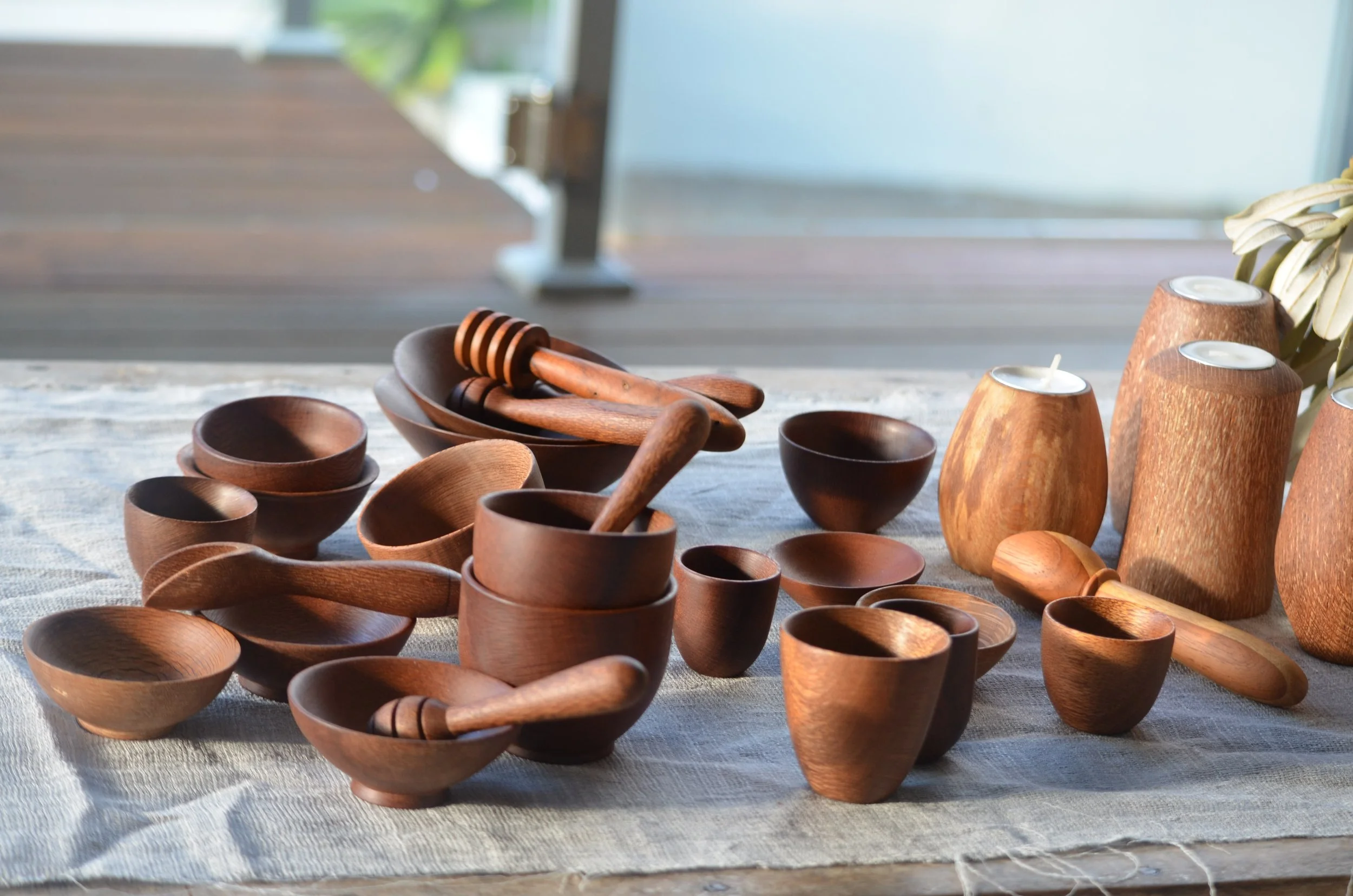 Collection of wooden bowls, spoons, honey dippers, and candles on a cloth-covered table.