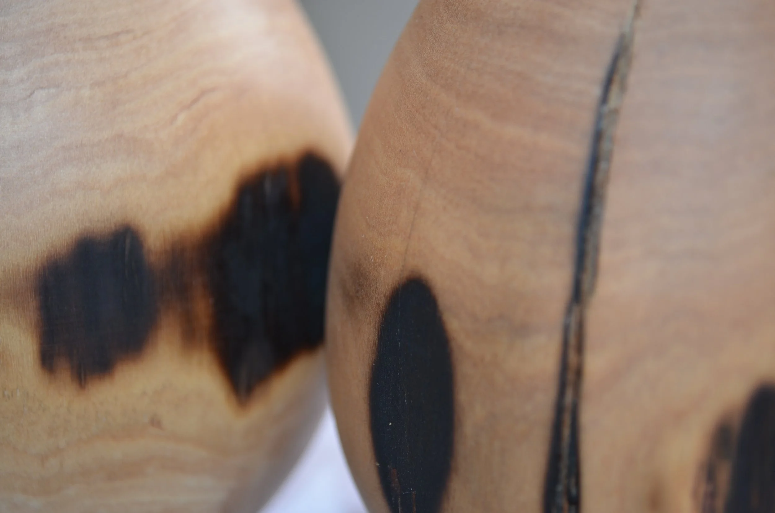 Close-up of a wooden surface with black burned or painted circular and irregular shapes.