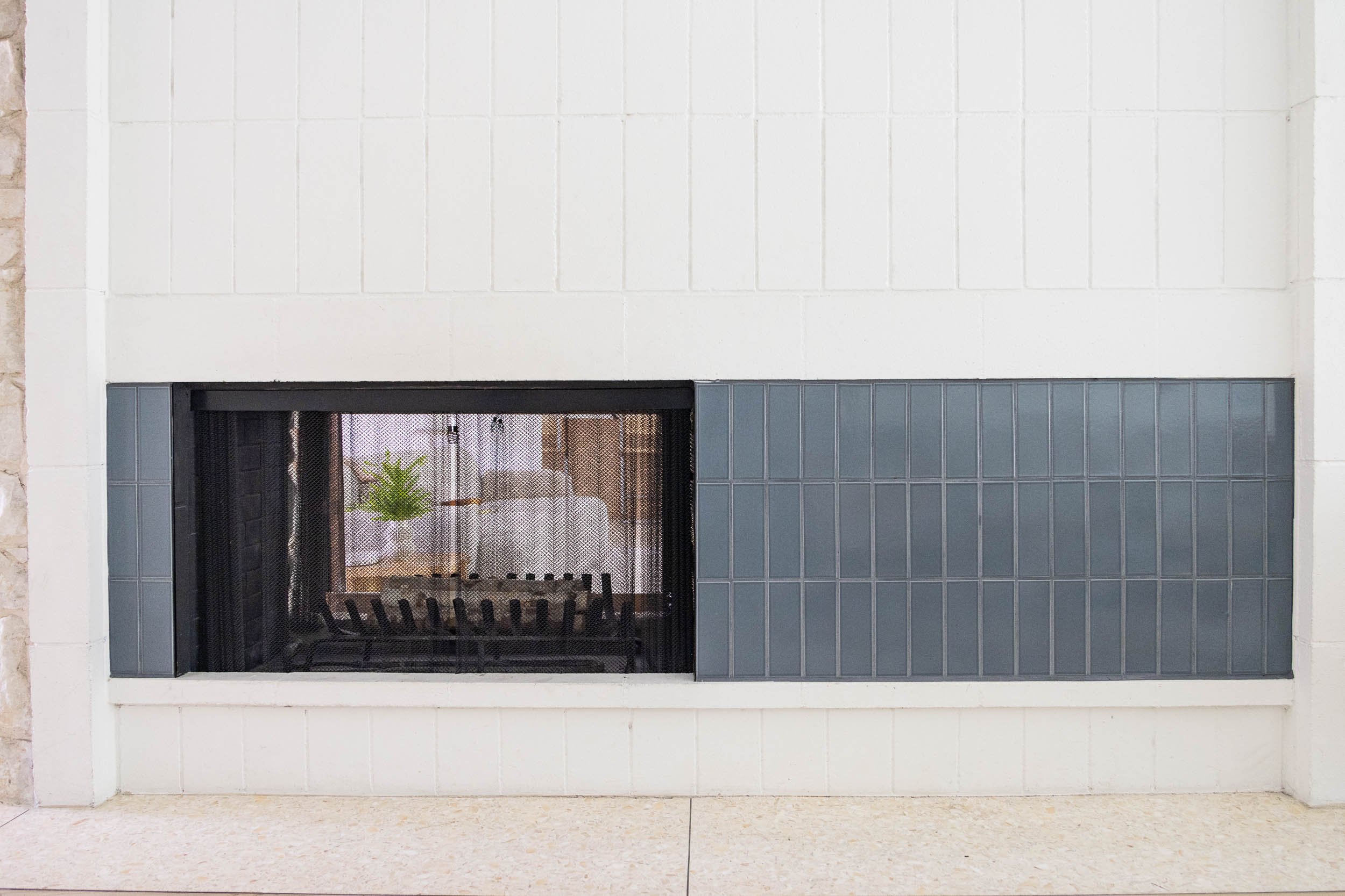 Modern fireplace with a black metal grate and gray tile surround set in a white wall.