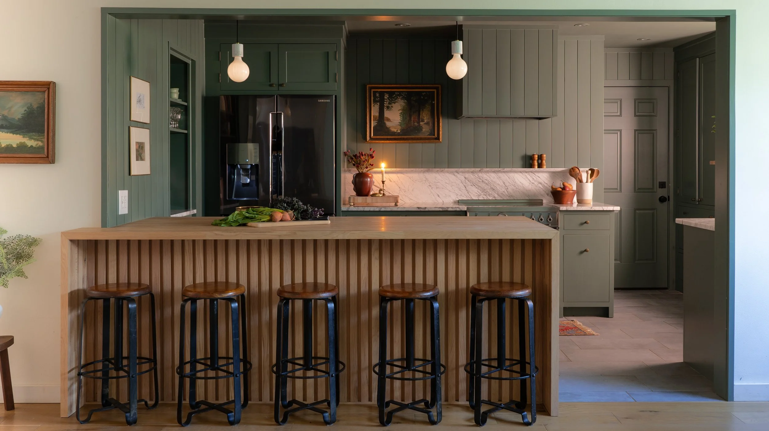 Sage green kitchen remodel in Austin with a fluted white oak island, black counter stools, pendant lights and a stone backsplash