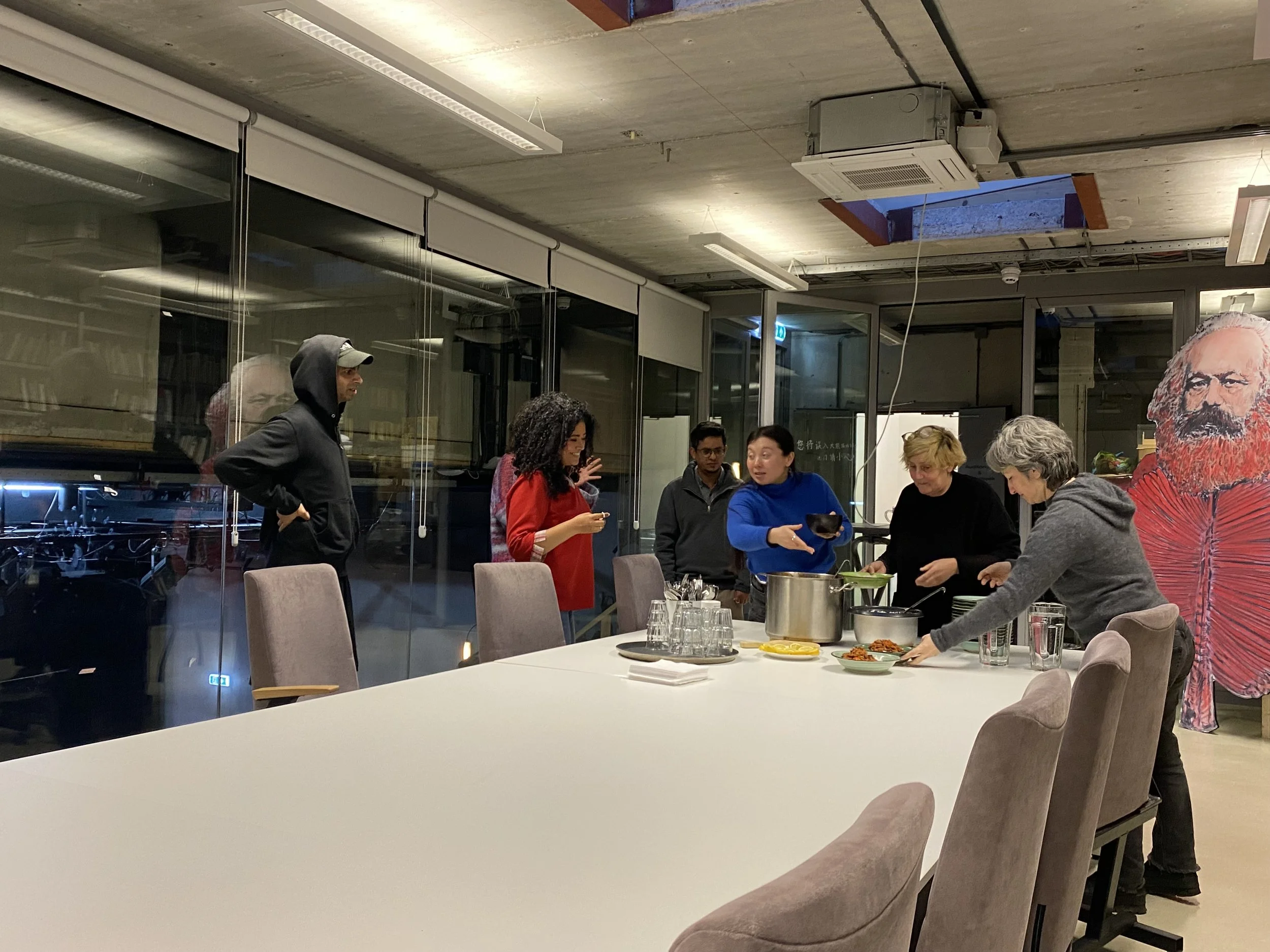 Enthousiastic group of people on the end of a big white table, gathering food and talking to each other.