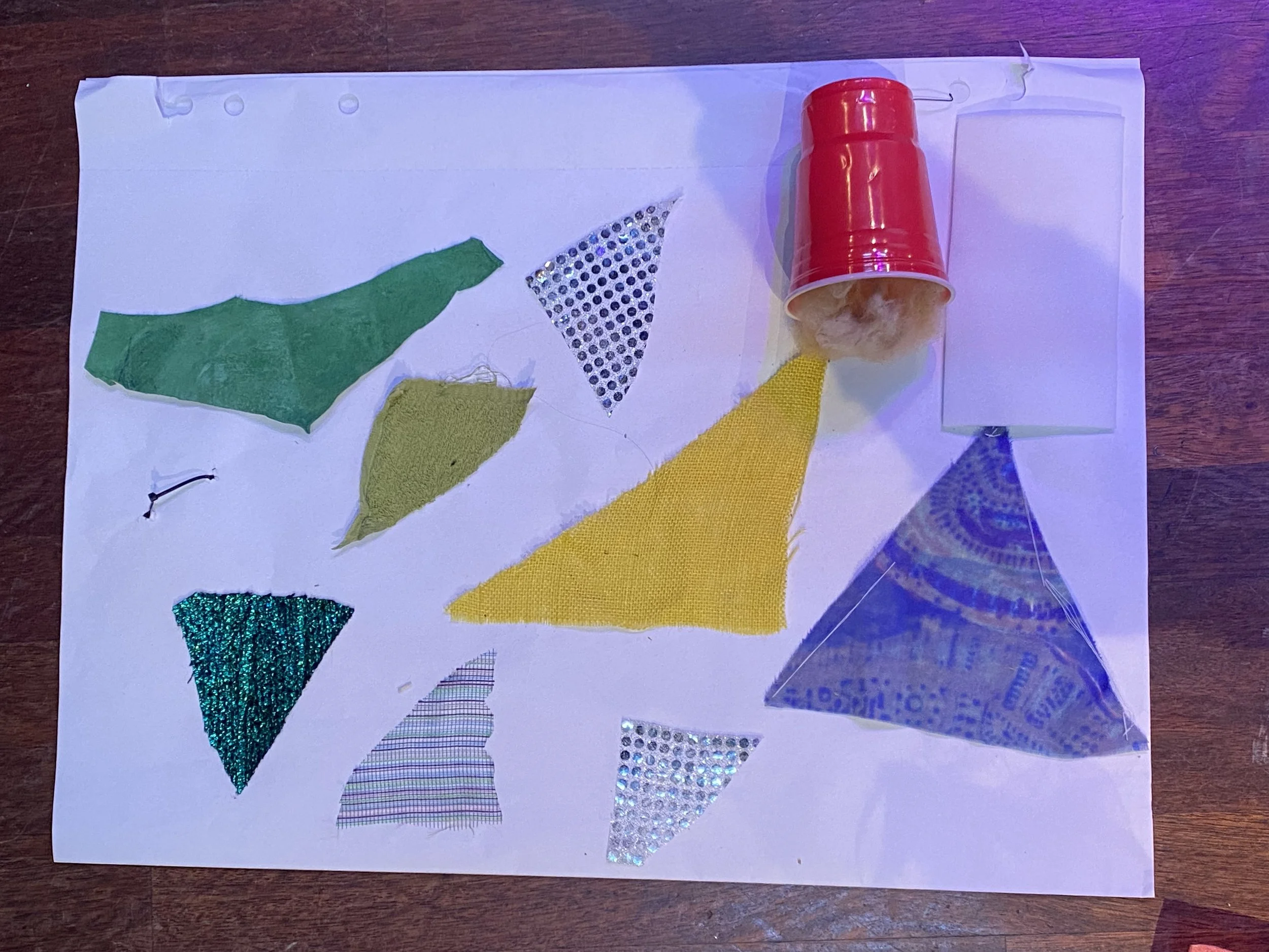 White piece of paper with colorful cut-out triangles on the paper. A red fallen cup on the paper. It looks like the cup is spilling the colorful triangles.