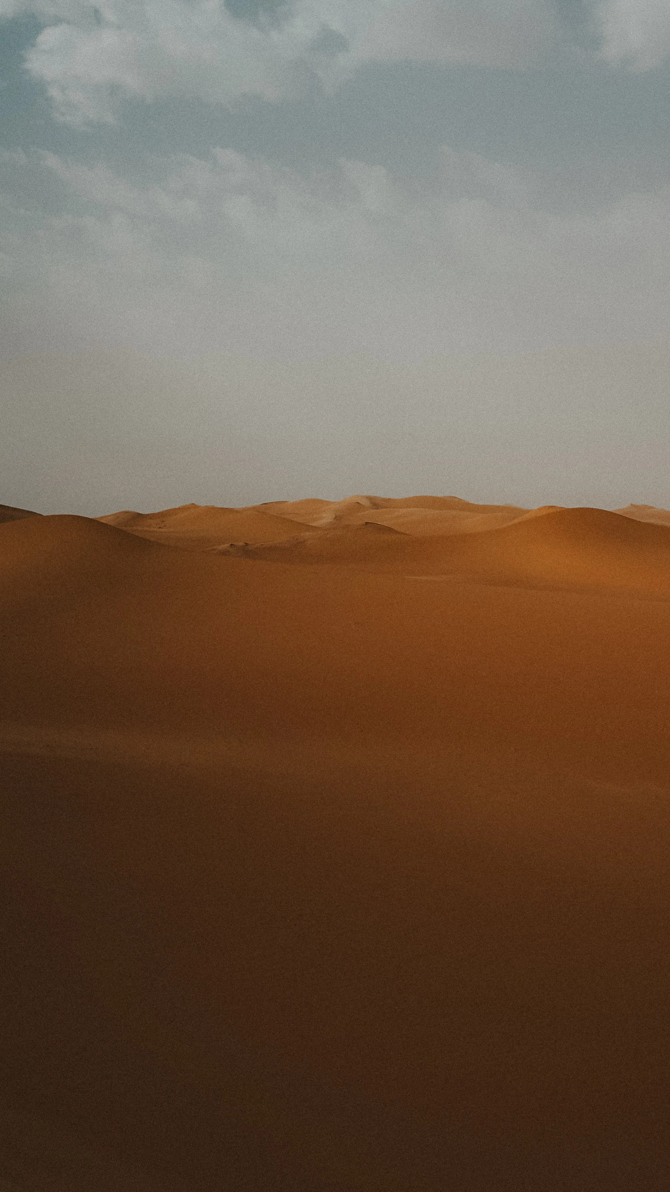 Desert landscape with rolling sand dunes under a partly cloudy sky.