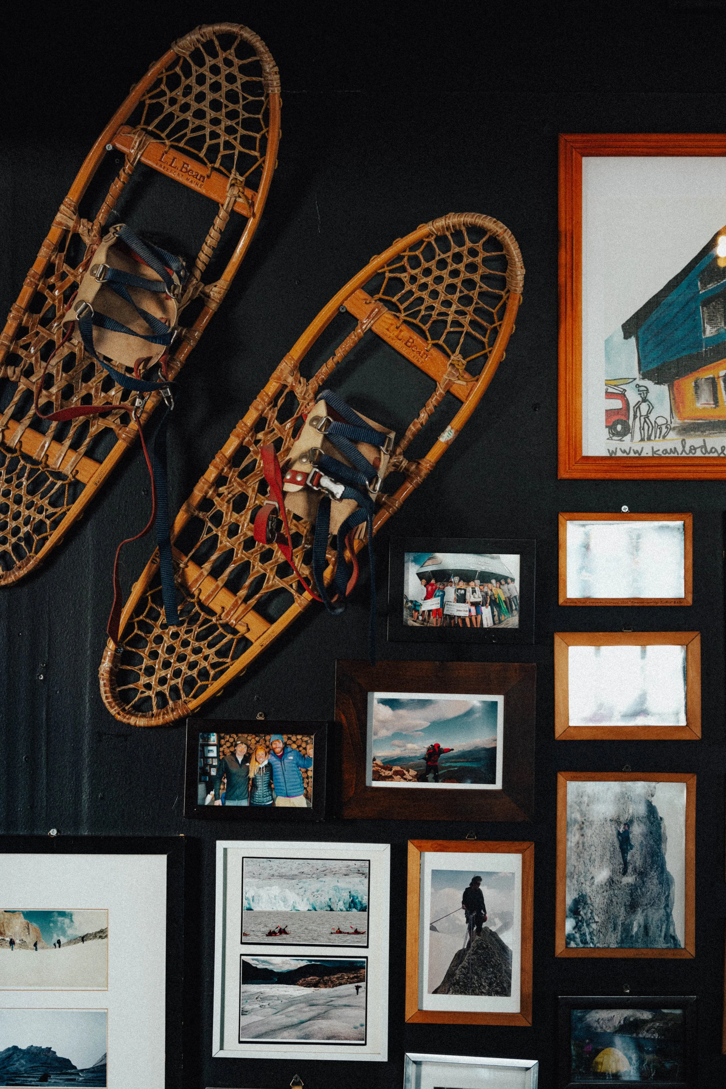 A black wall decorated with vintage wooden snowshoes, framed photographs of outdoor adventures, and colorful artwork.