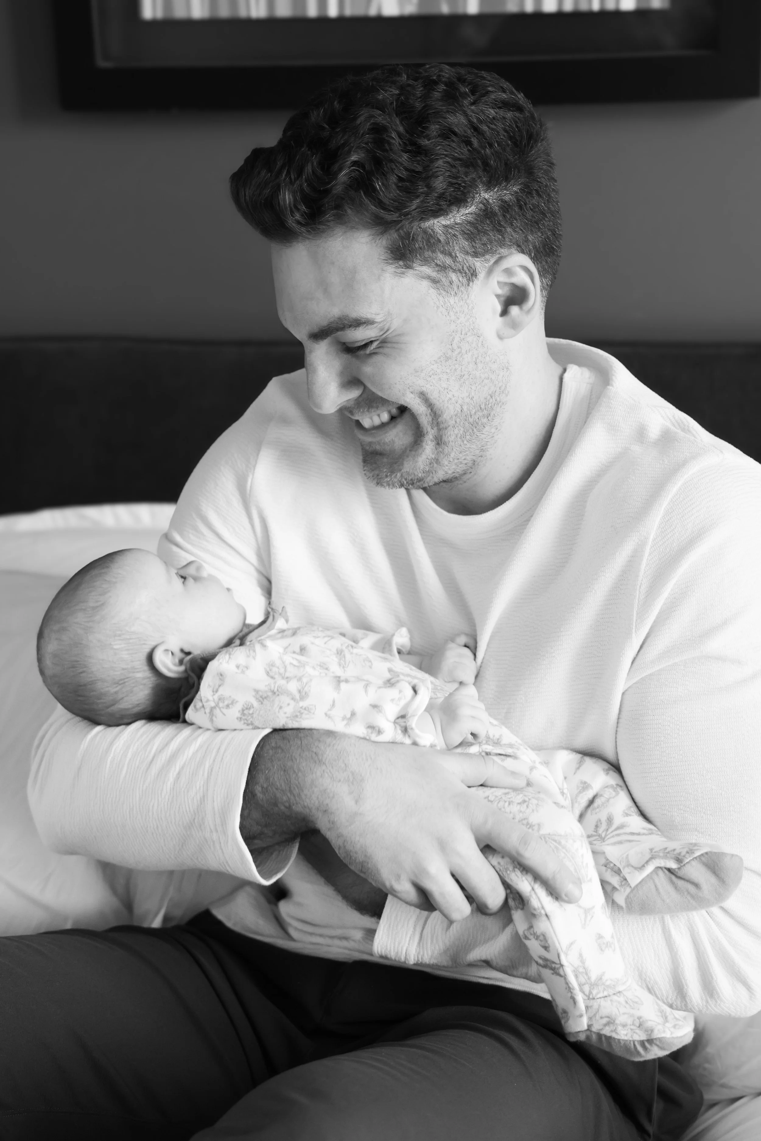 A man holding a baby in his arms, smiling at the baby, in a cozy indoor setting.