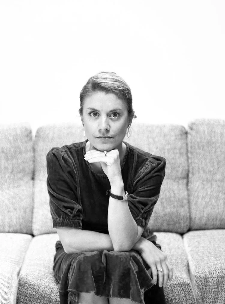 Black and white photo of a woman sitting on a sofa with her chin resting on her hand, looking directly at the camera.