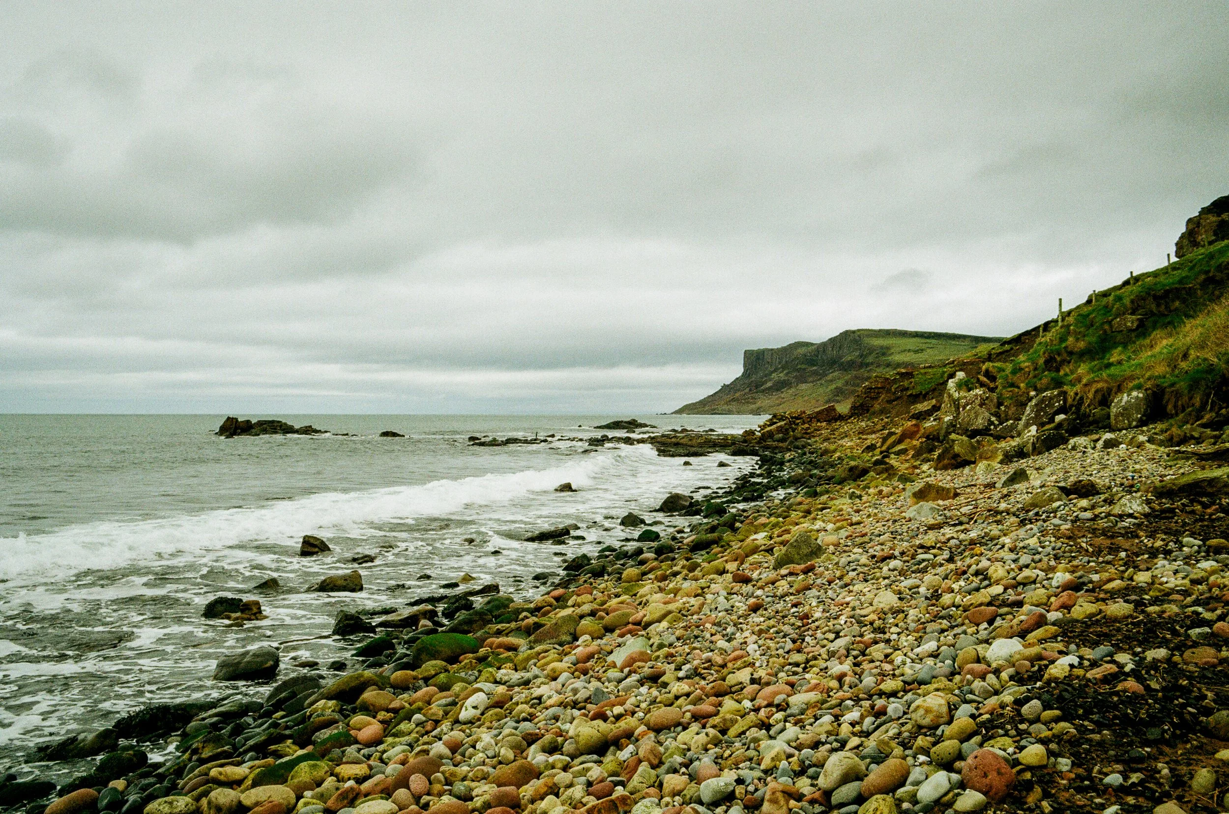 Rocky beach with gray clouds overhead and cliffs in the distance.