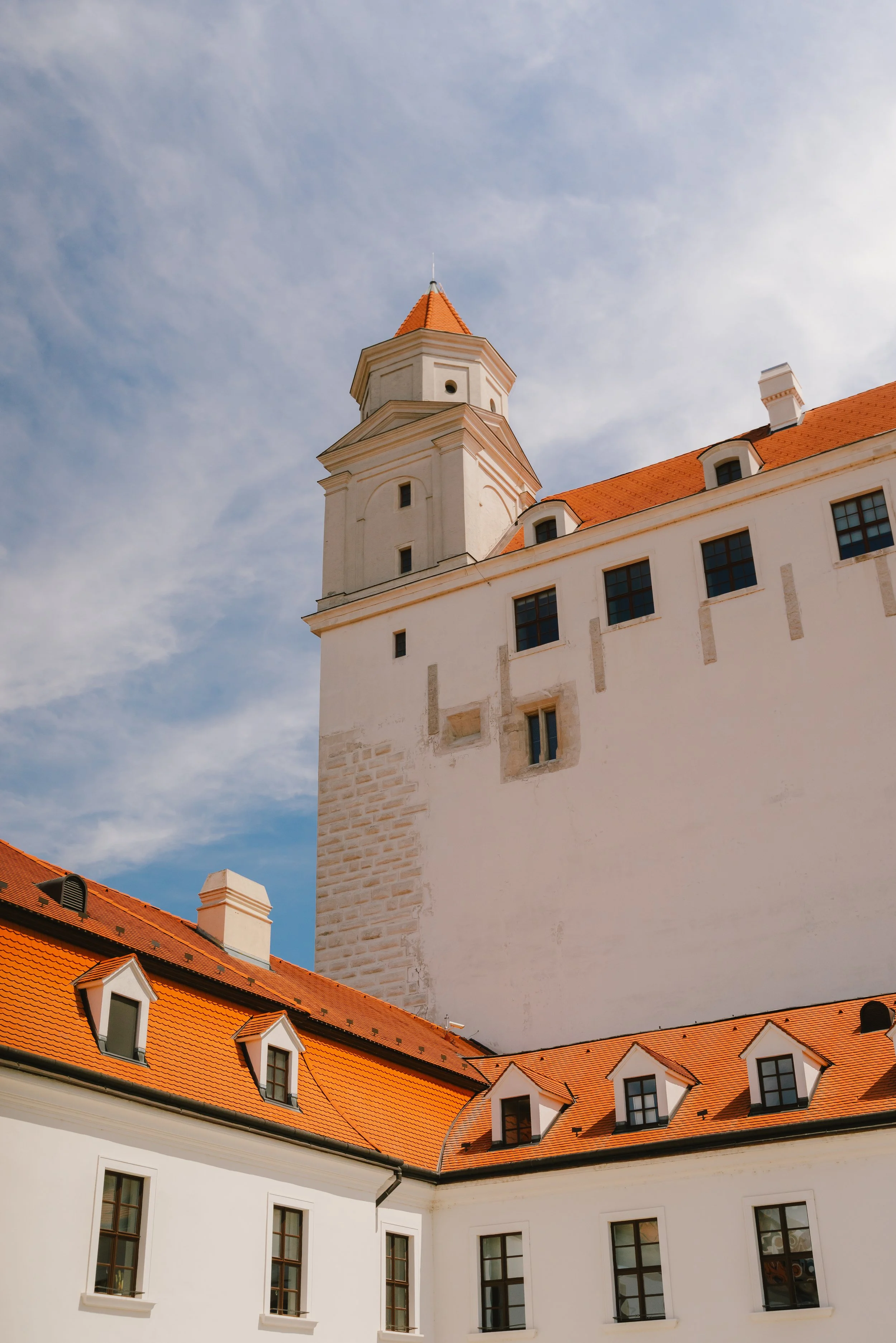 A castle with white walls and red-tile roofs under a blue sky with scattered clouds.