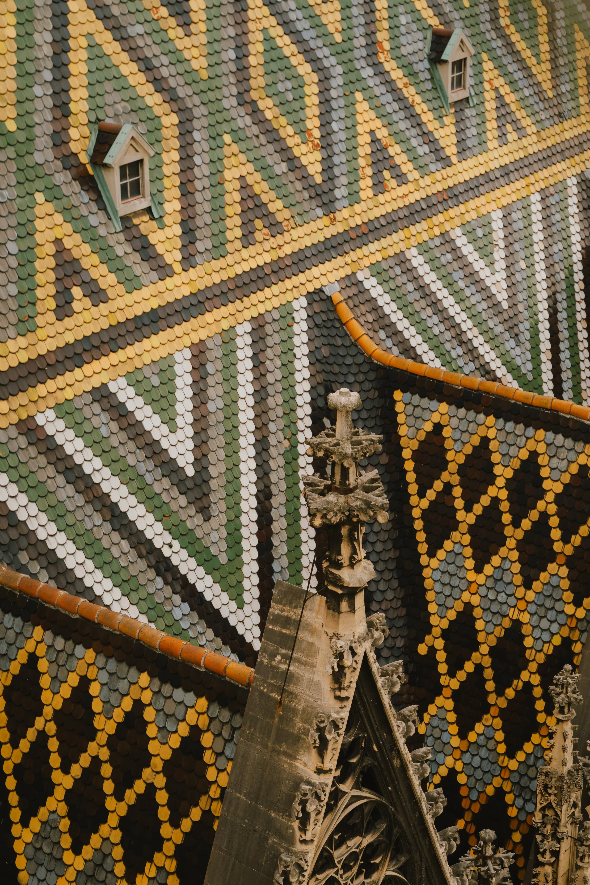 Close-up view of a colorful, intricately patterned roof of a historic Gothic-style building, featuring small, overlapping, multicolored tiles and small dormer windows.