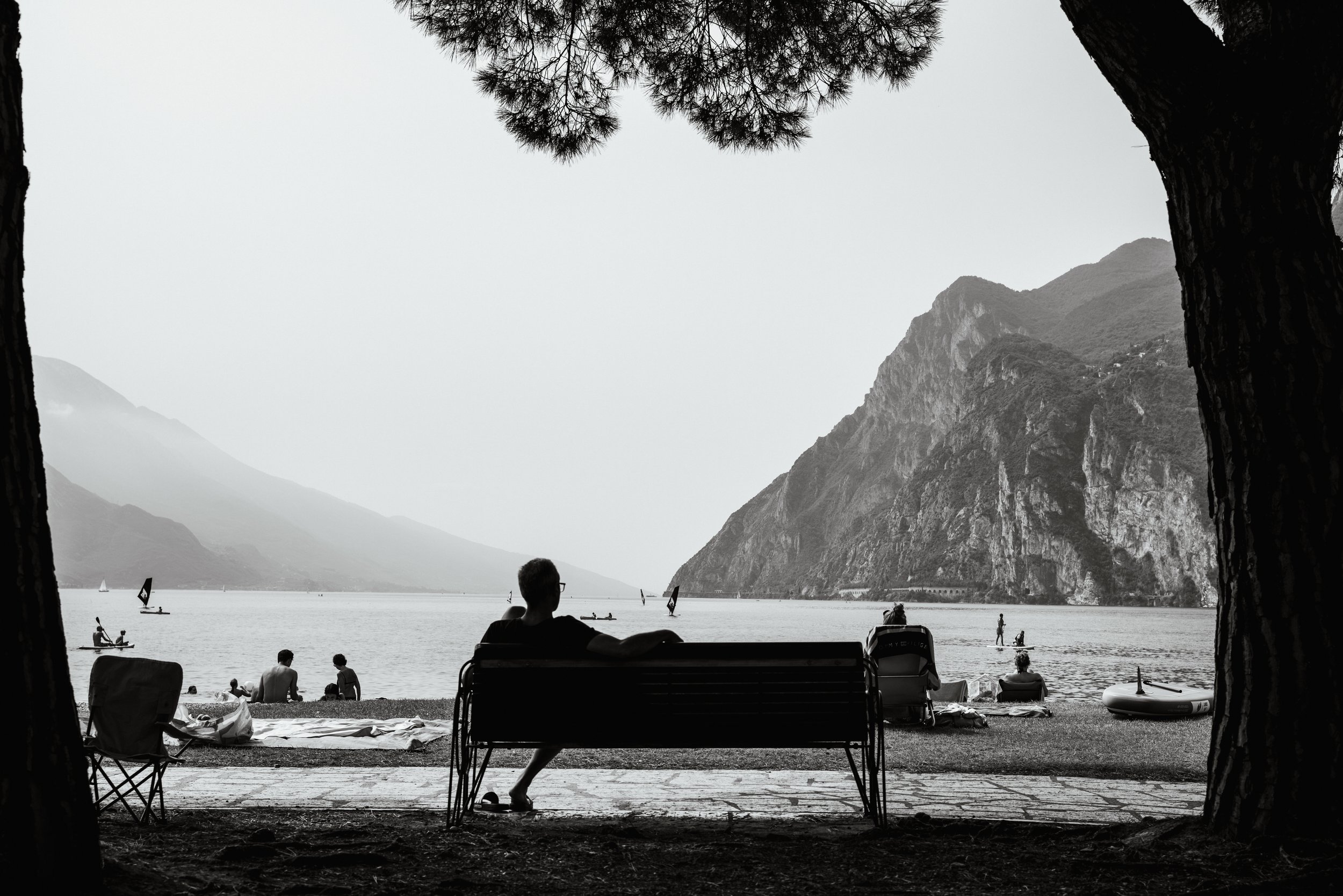 Black and White image of a lone male sat on a bench at the beach on Lake Garda