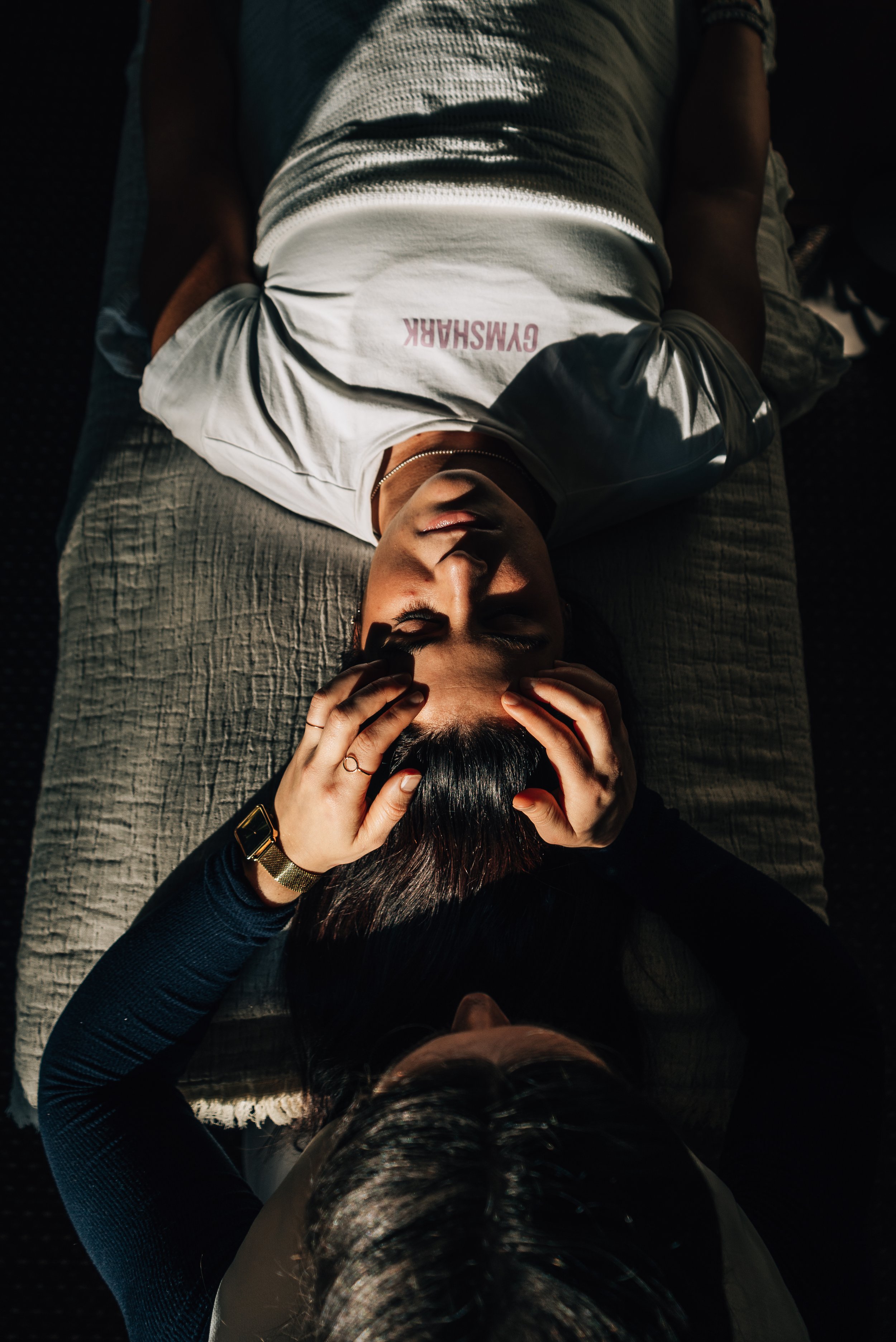 A person lying on a bed with hands on their head, another person touching their hair.