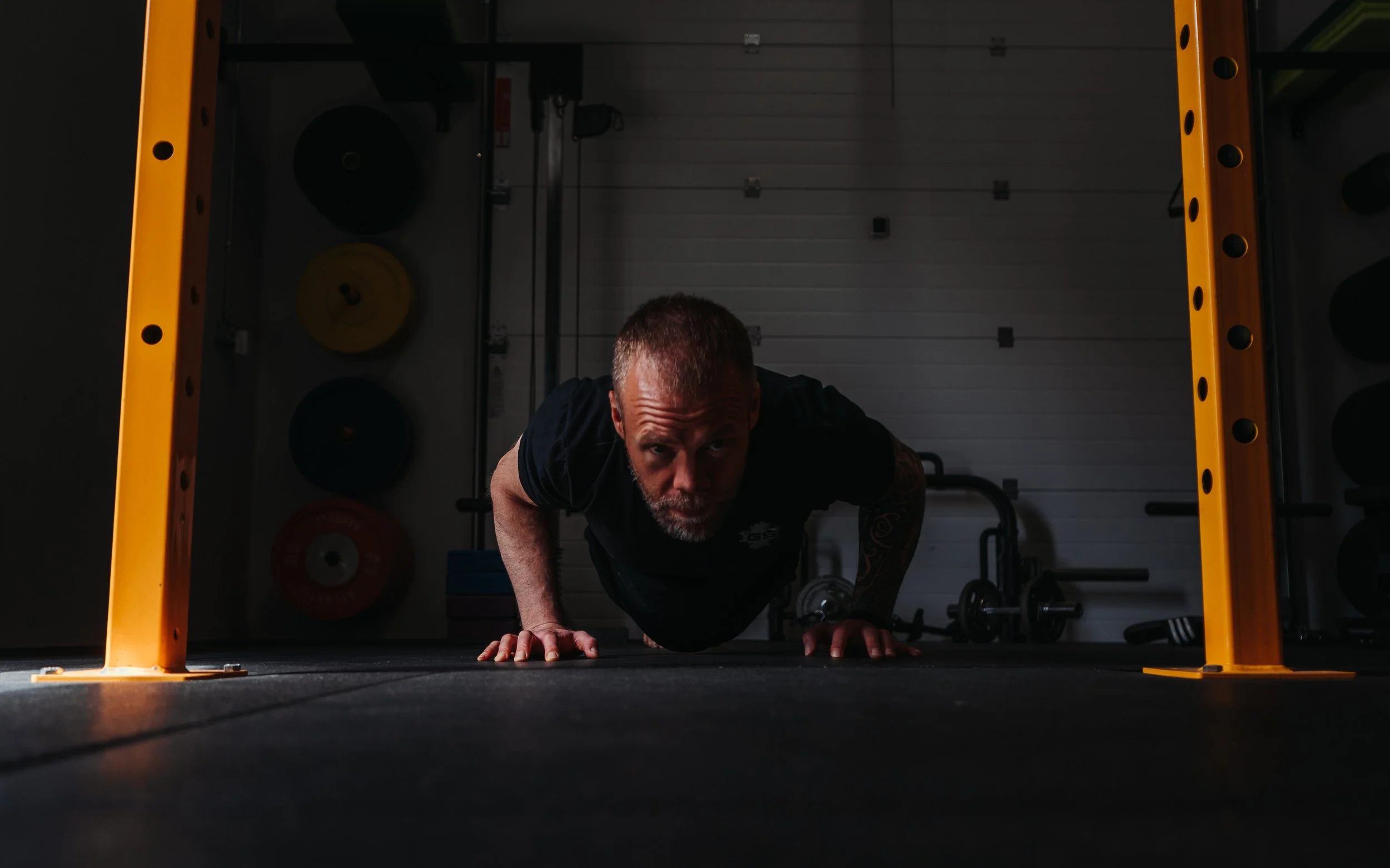 A man performs a push-up exercise in a gym, viewed from a low angle with equipment in the background.