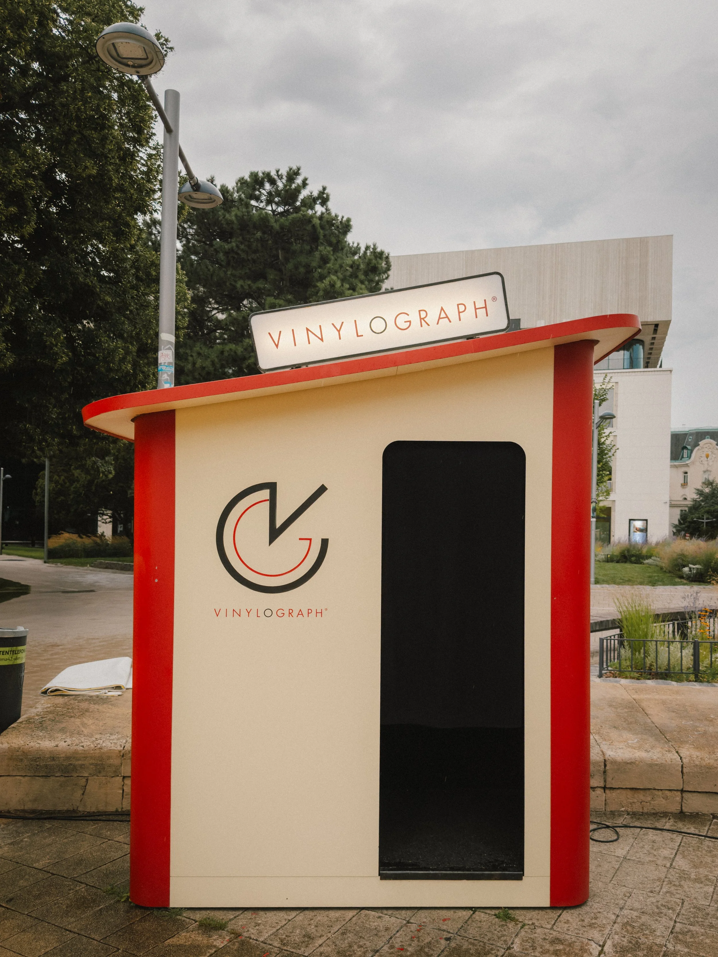 Photo of a vending machine branded with Vinylograph logo and name, with a black opening for placing records or items, situated outdoors under cloudy sky.