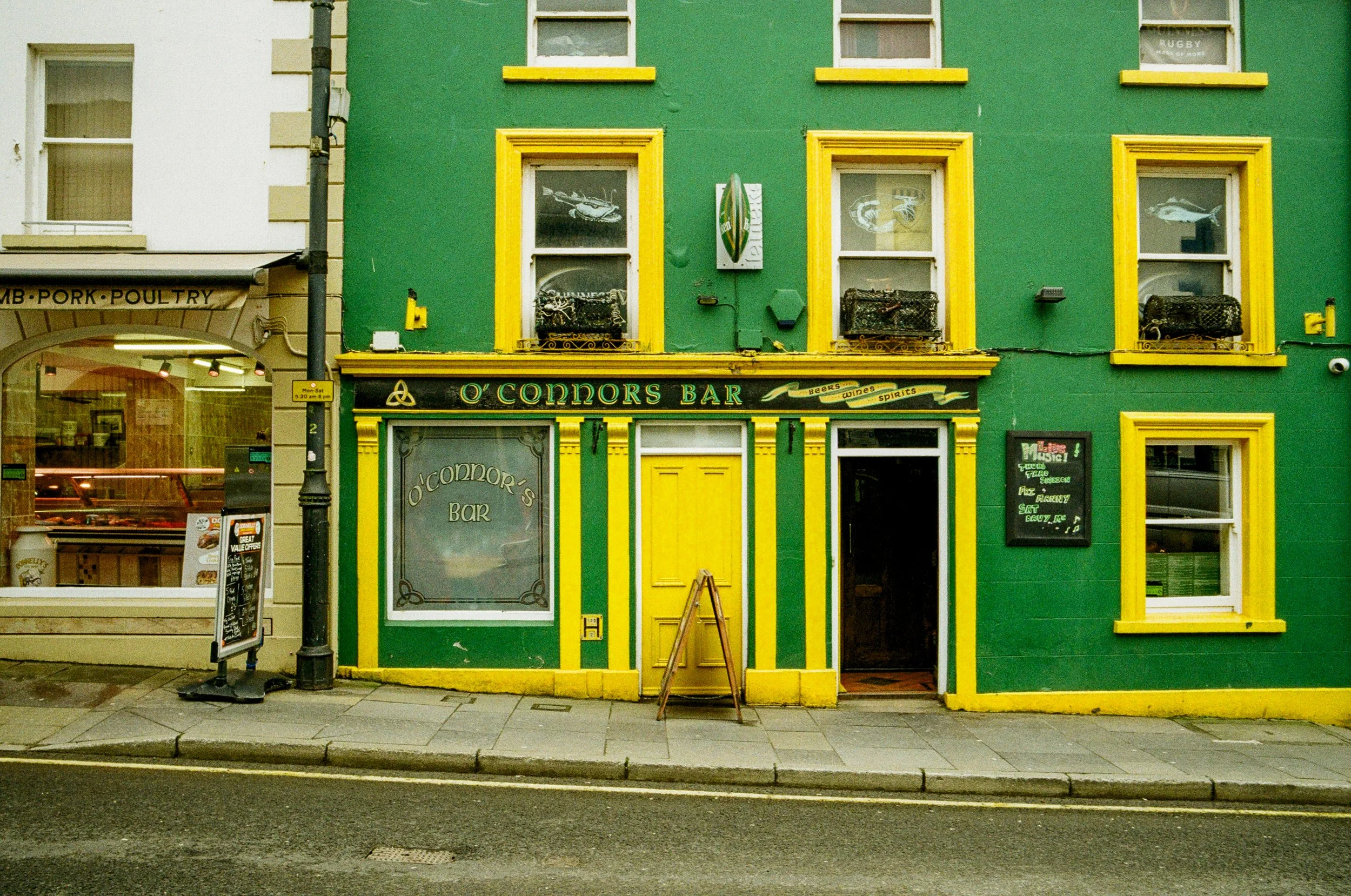 A brightly colored green building with yellow trim housing O'Connors Bar. The bar's sign and entrance are visible, with a sidewalk in front. There is a blackboard menu outside the bar.