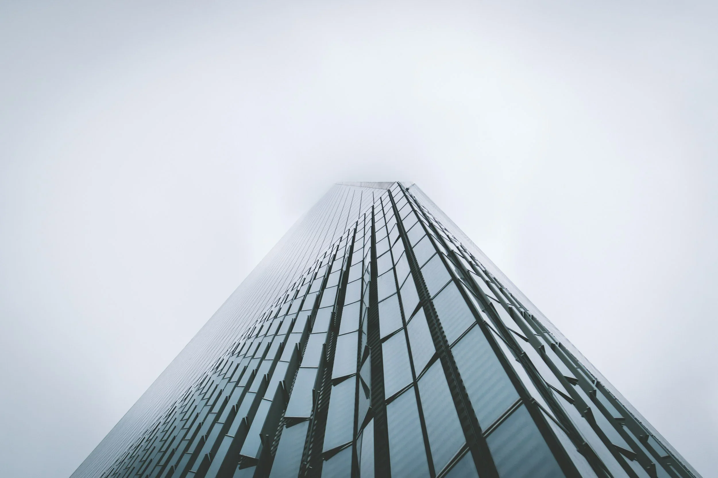 Low-angle view of a modern glass skyscraper reaching into the cloudy sky.