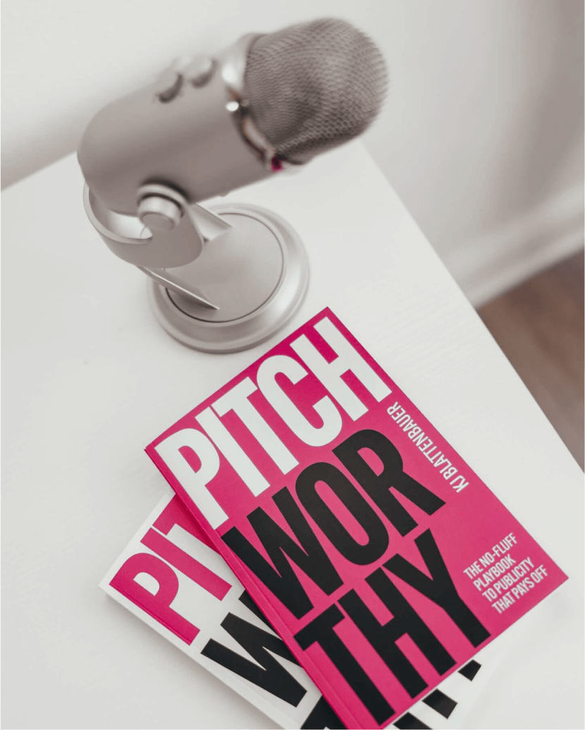 A white microphone on a stand and two pink and black books titled 'Pitchworthy'