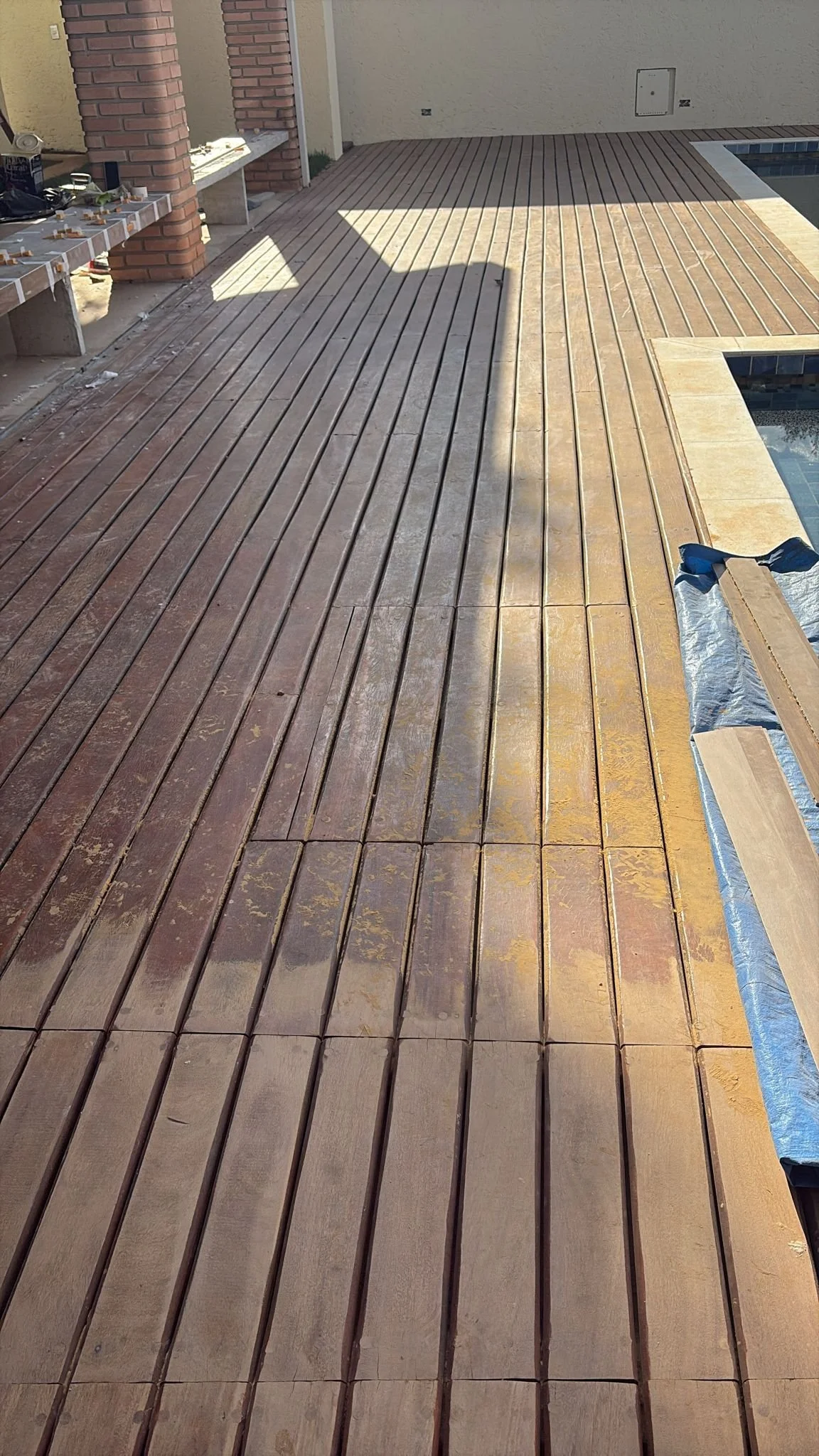 Transitioning wooden deck with darker stained section on the left and lighter finished section on the right, near a pool.