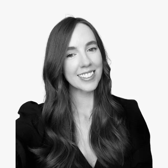 Black-and-white portrait of a woman with long wavy hair, smiling at the camera, wearing a dark top.