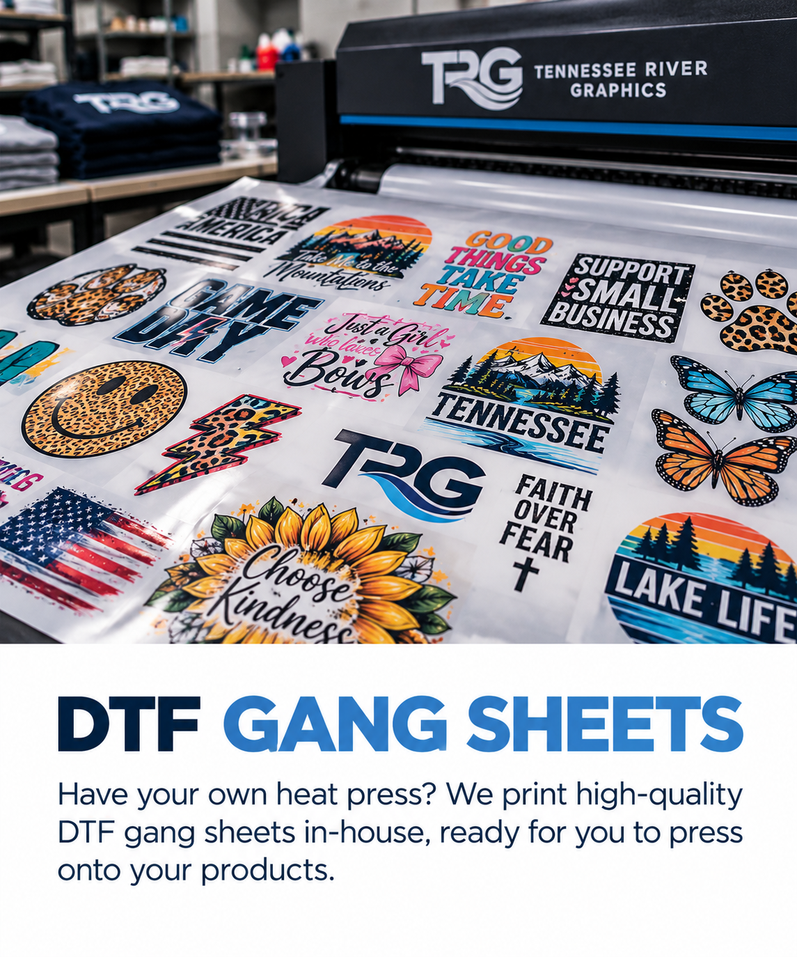 Display of various colorful DTF gang sheets with designs including mountains, butterflies, flowers, smiley faces, American flag, and text promoting positivity and small business support, on a heat press machine in a printing shop.