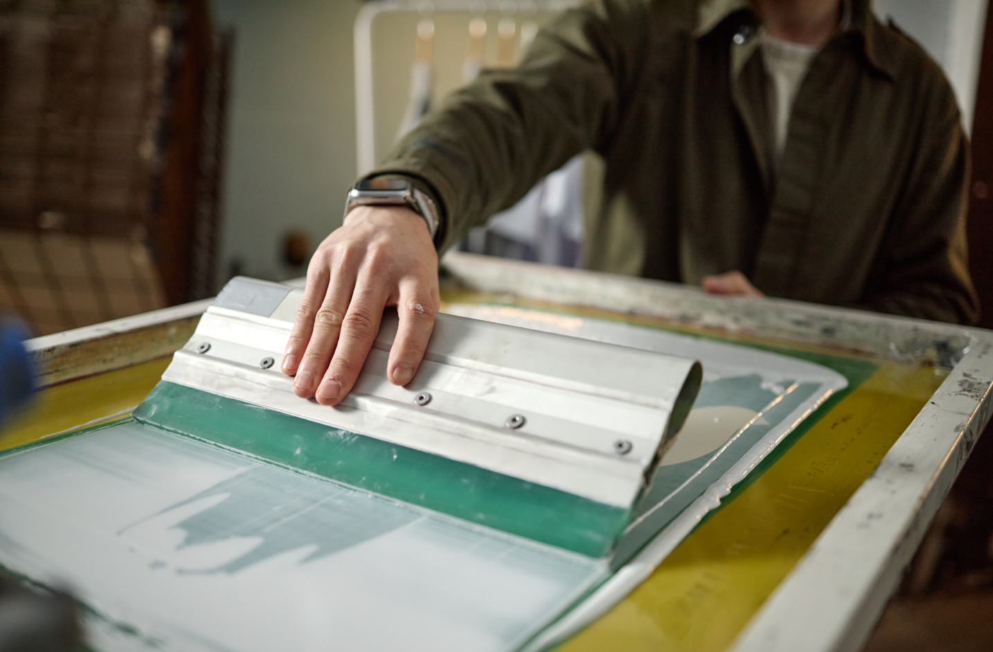 Person handling a screen printing frame with green ink on a printing table.
