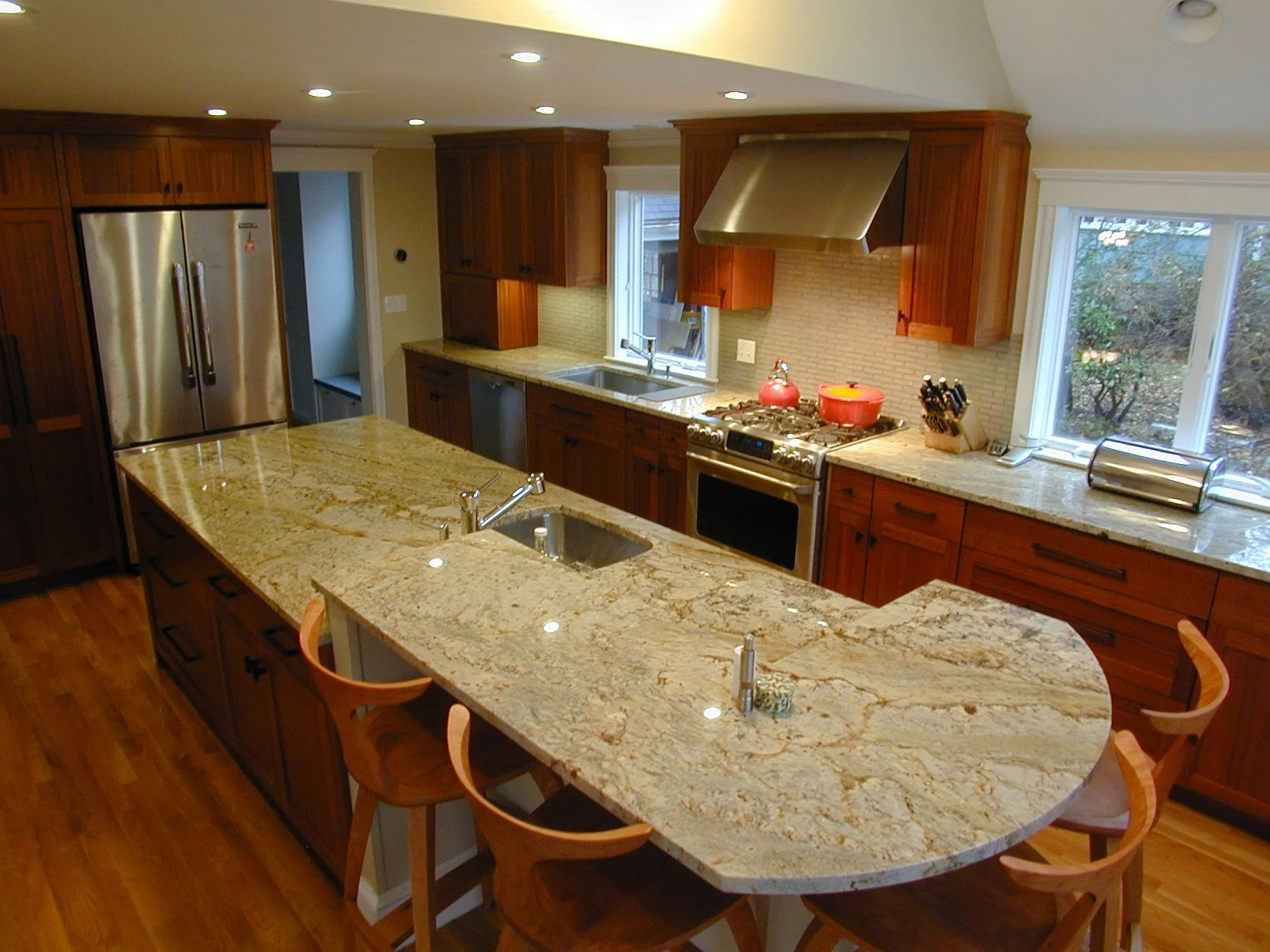 A spacious kitchen with wooden cabinets, a large granite island with a sink, stainless steel appliances, and a window looking outside.
