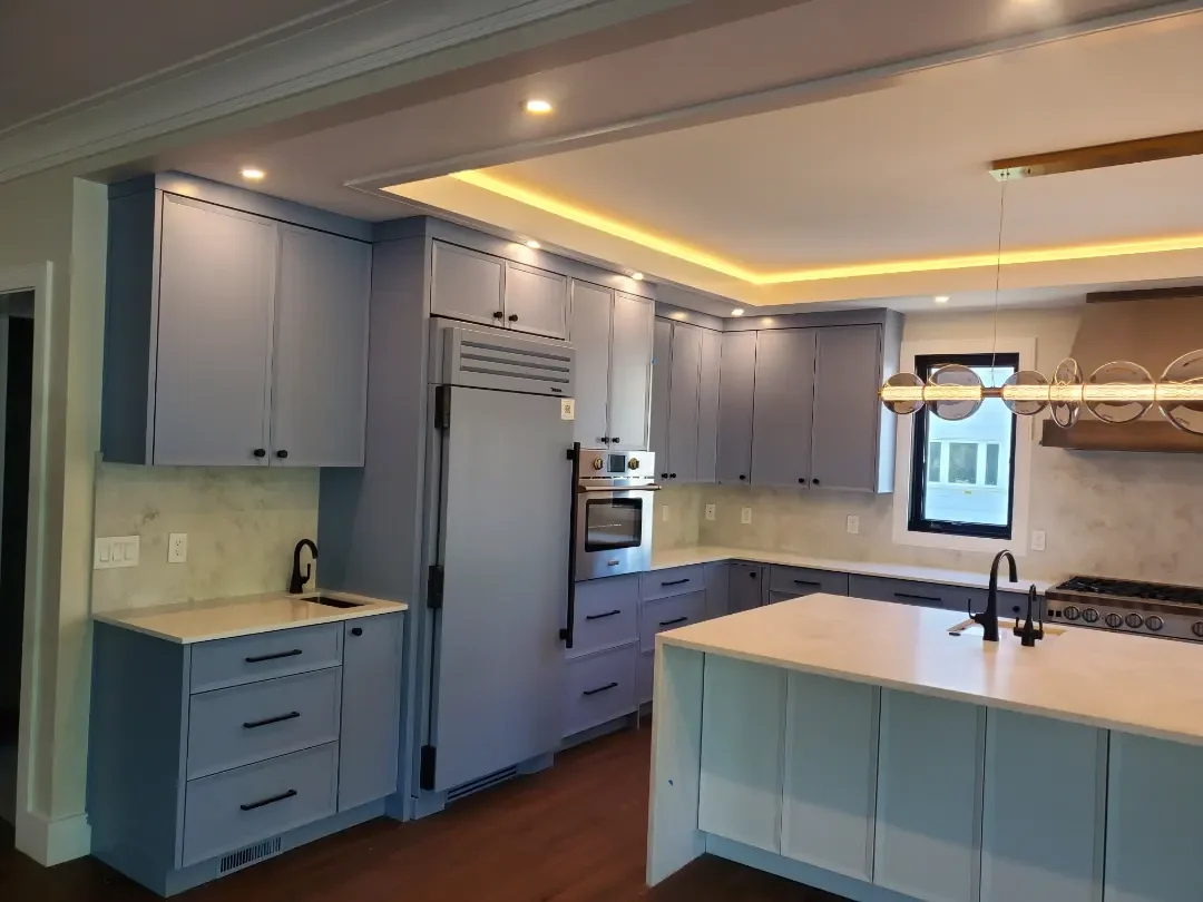 A modern kitchen with blue cabinets, a marble backsplash, a kitchen island, and black fixtures. The kitchen has under-cabinet lighting and a pendant light fixture.