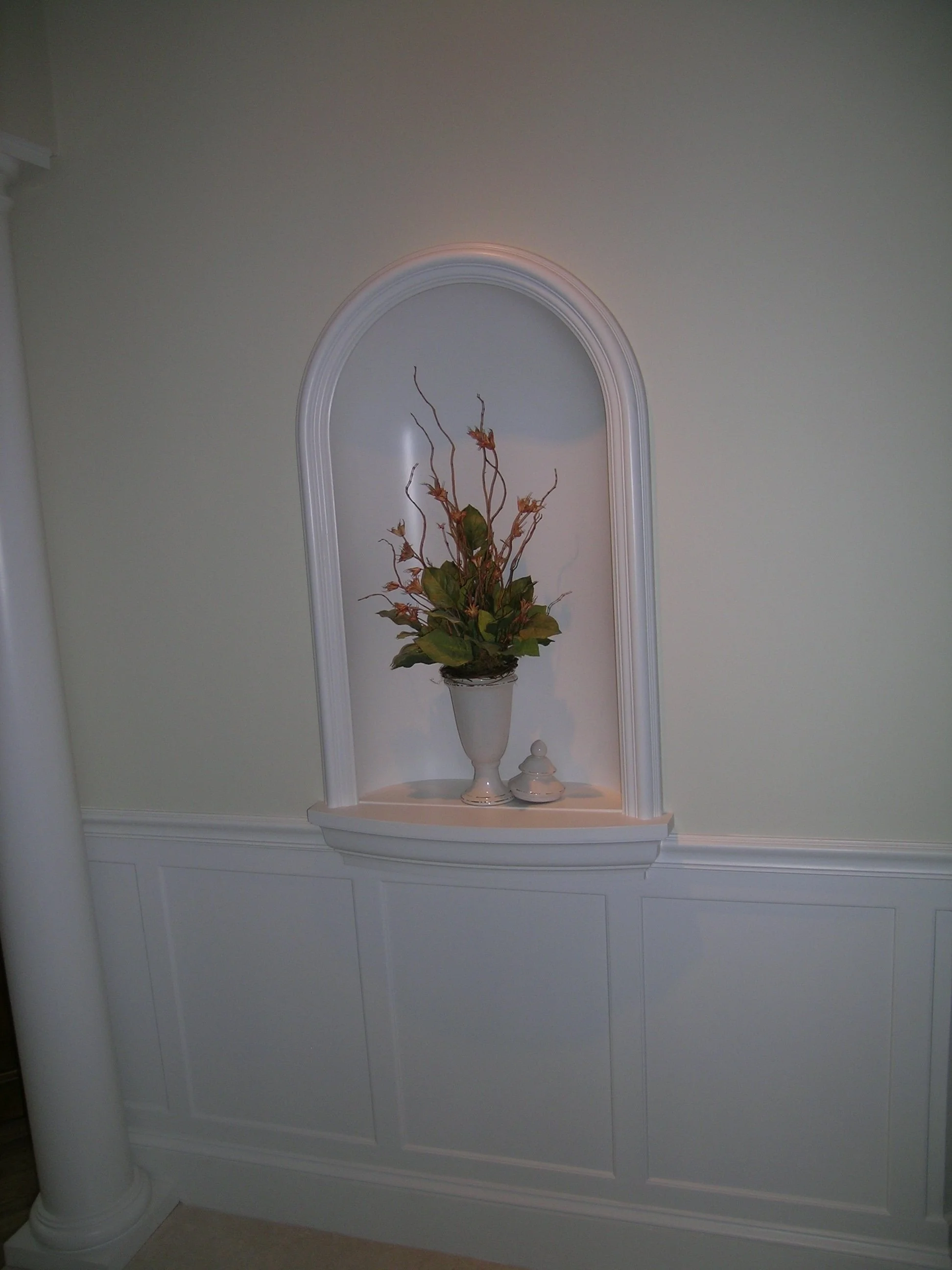 White decorative wall niche with floral arrangement and small decorative object.