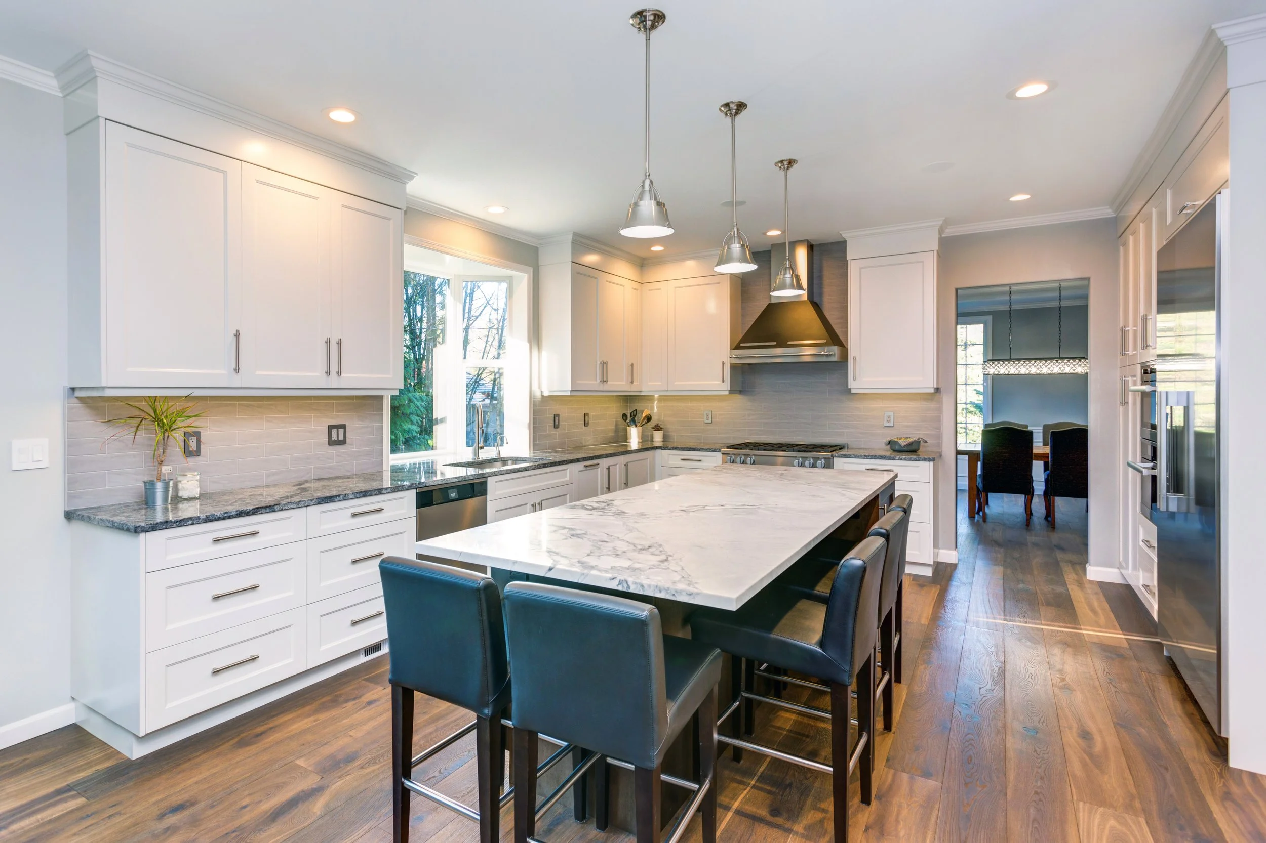 Modern kitchen with white cabinets, marble island, and hardwood floors.