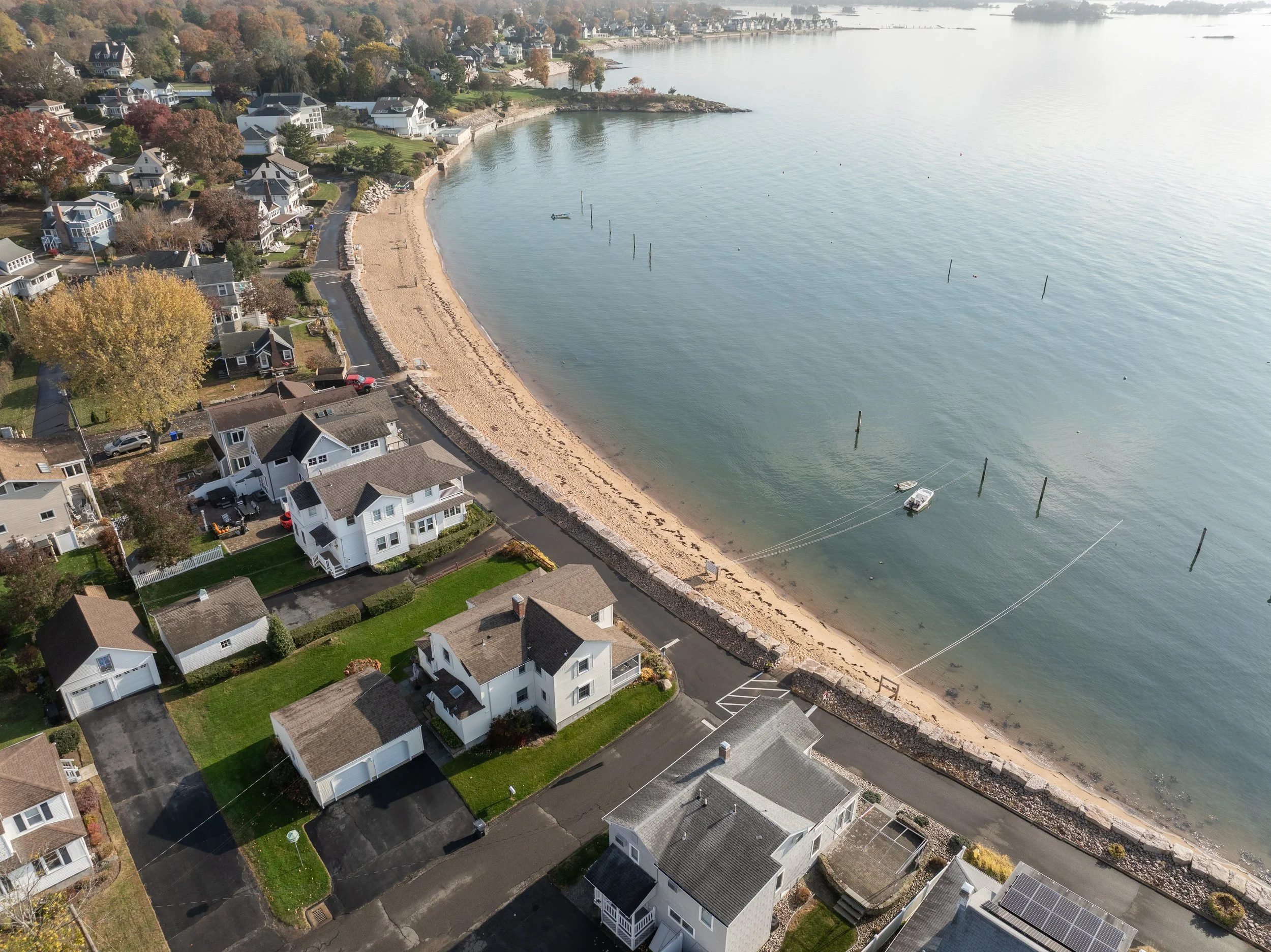 An aerial view of a residential neighborhood along a curved beach with several boats anchored off the shore.
